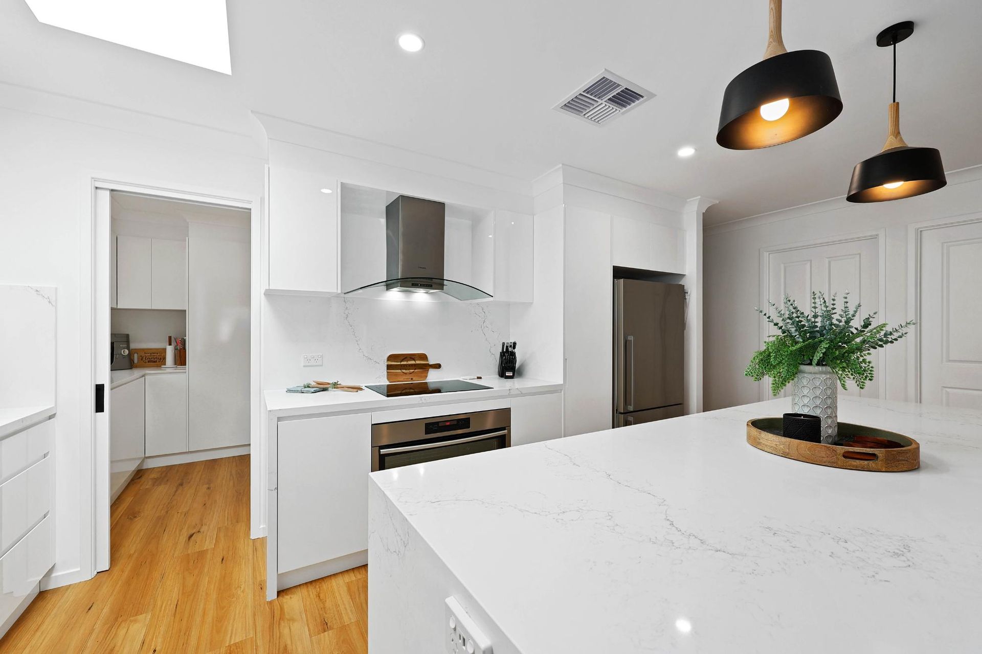 Modern White Kitchen with Island, Hardwood Floors, Stainless Steel Appliances, and Pendant Lights — Above & Beyond Interiors Custom Joinery in Wattle Grove, NSW