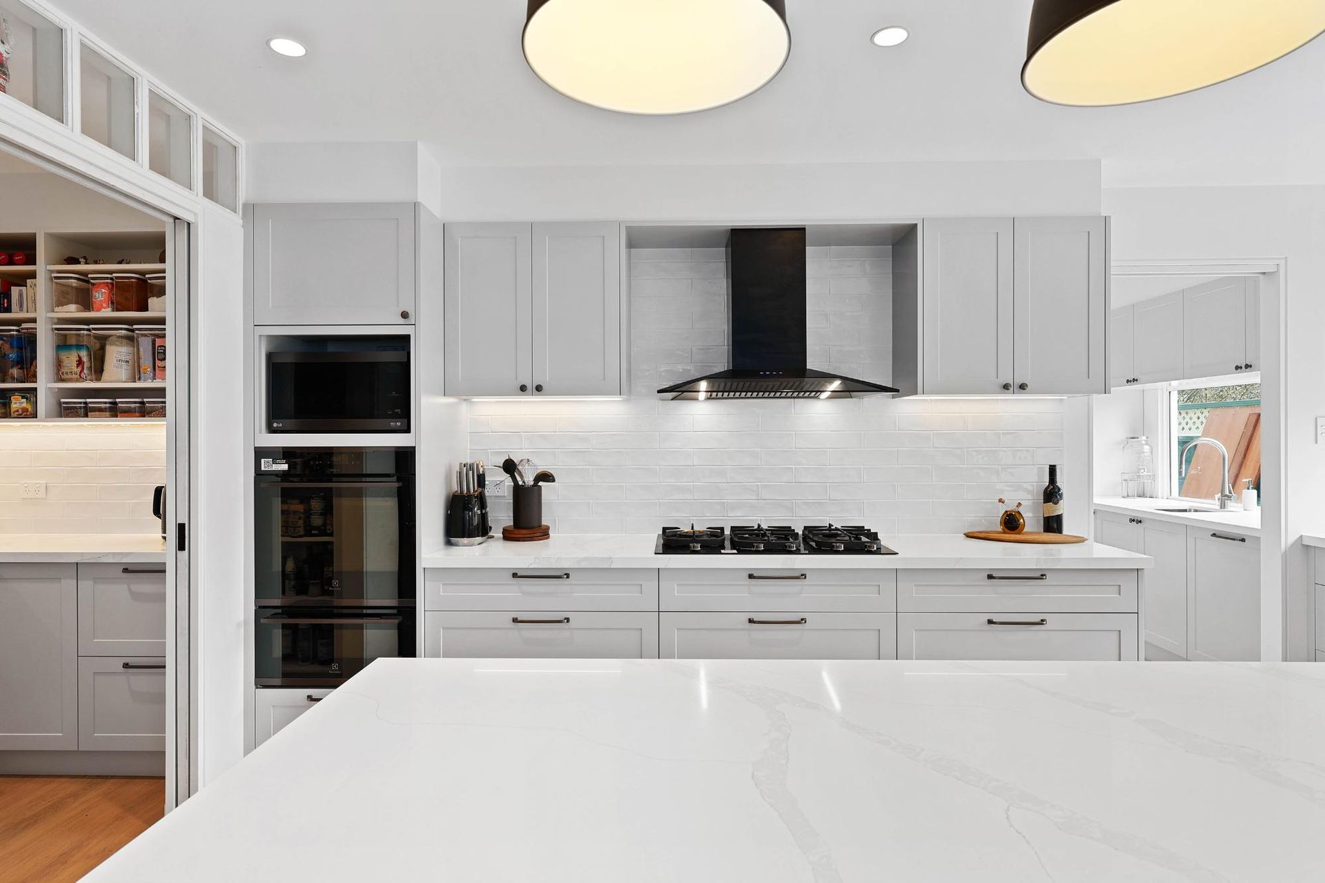 Modern White Kitchen with Grey Cabinets, Black Range Hood, and White Countertop — Above & Beyond Interiors Custom Joinery in Yowie Bay, NSW