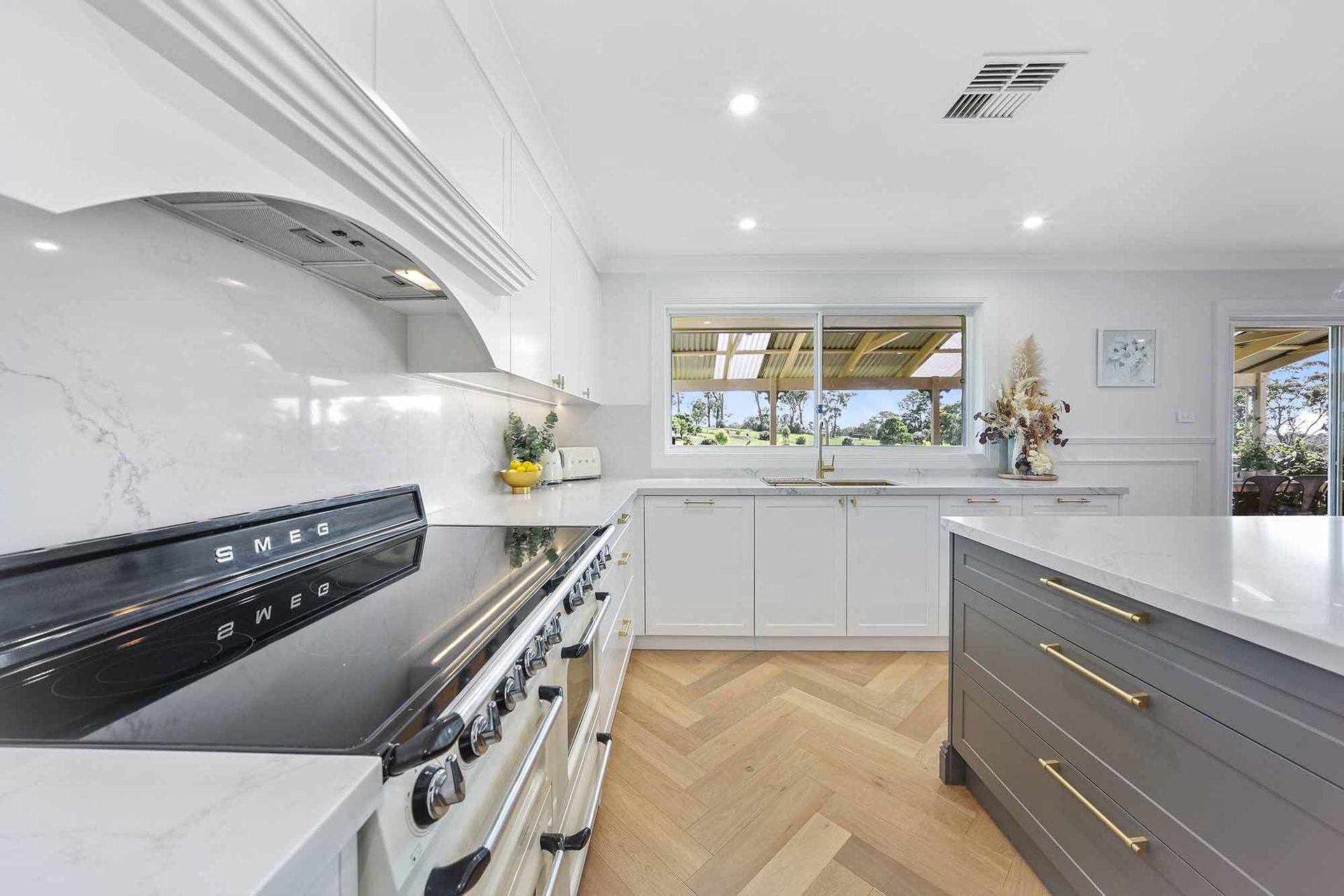 Modern white kitchen with grey island, herringbone floors, and stainless steel appliances — Above & Beyond Interiors Custom Joinery in Bellambi, NSW