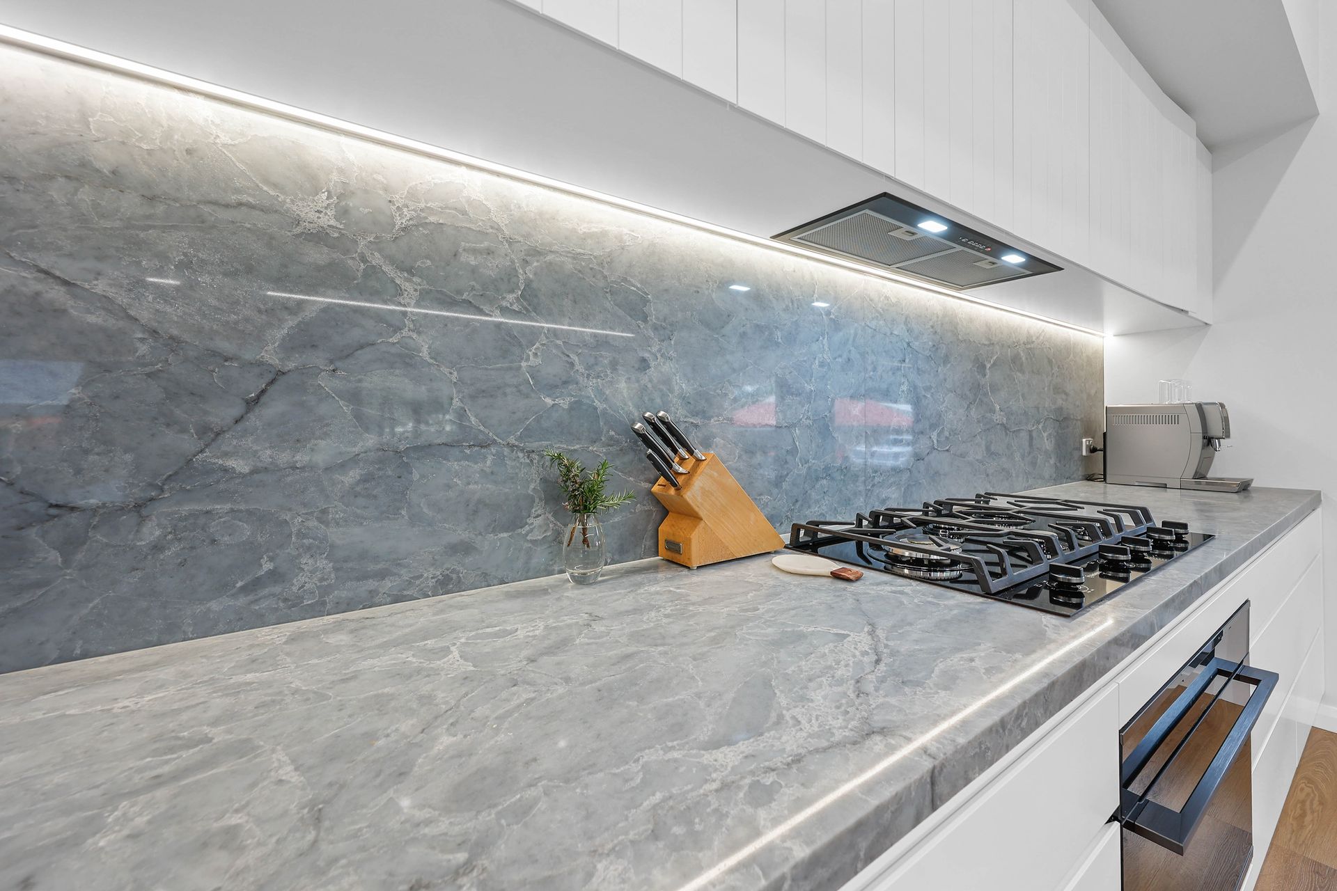 Grey marble kitchen countertop with a gas stove, backsplash, and upper cabinets — Above & Beyond Interiors Custom Joinery in Bellambi, NSW