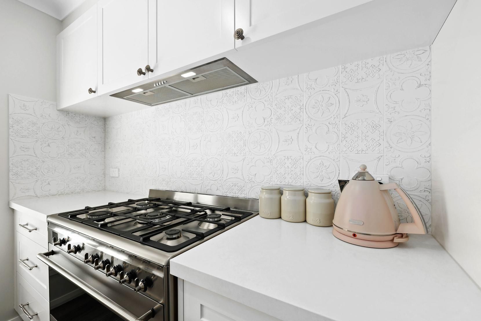 White Kitchen with Stove, Cabinets, Speckled Backsplash, and Pink Kettle — Above & Beyond Interiors Custom Joinery in Thirlmere, NSW