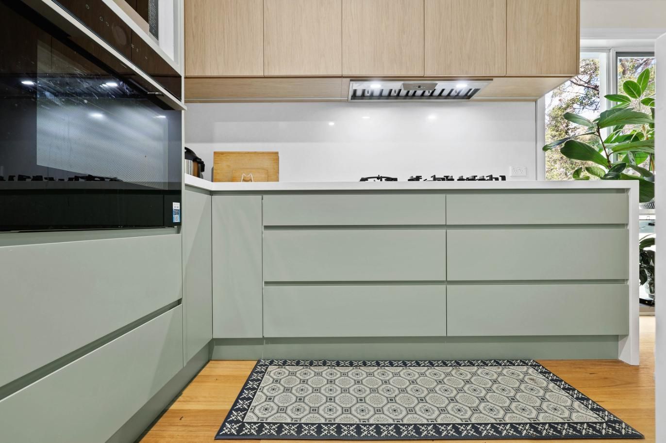 Modern Kitchen with Light Green Cabinets, Light Wood Upper Cabinets, and Patterned Rug — Above & Beyond Interiors Custom Joinery in Holsworthy, NSW