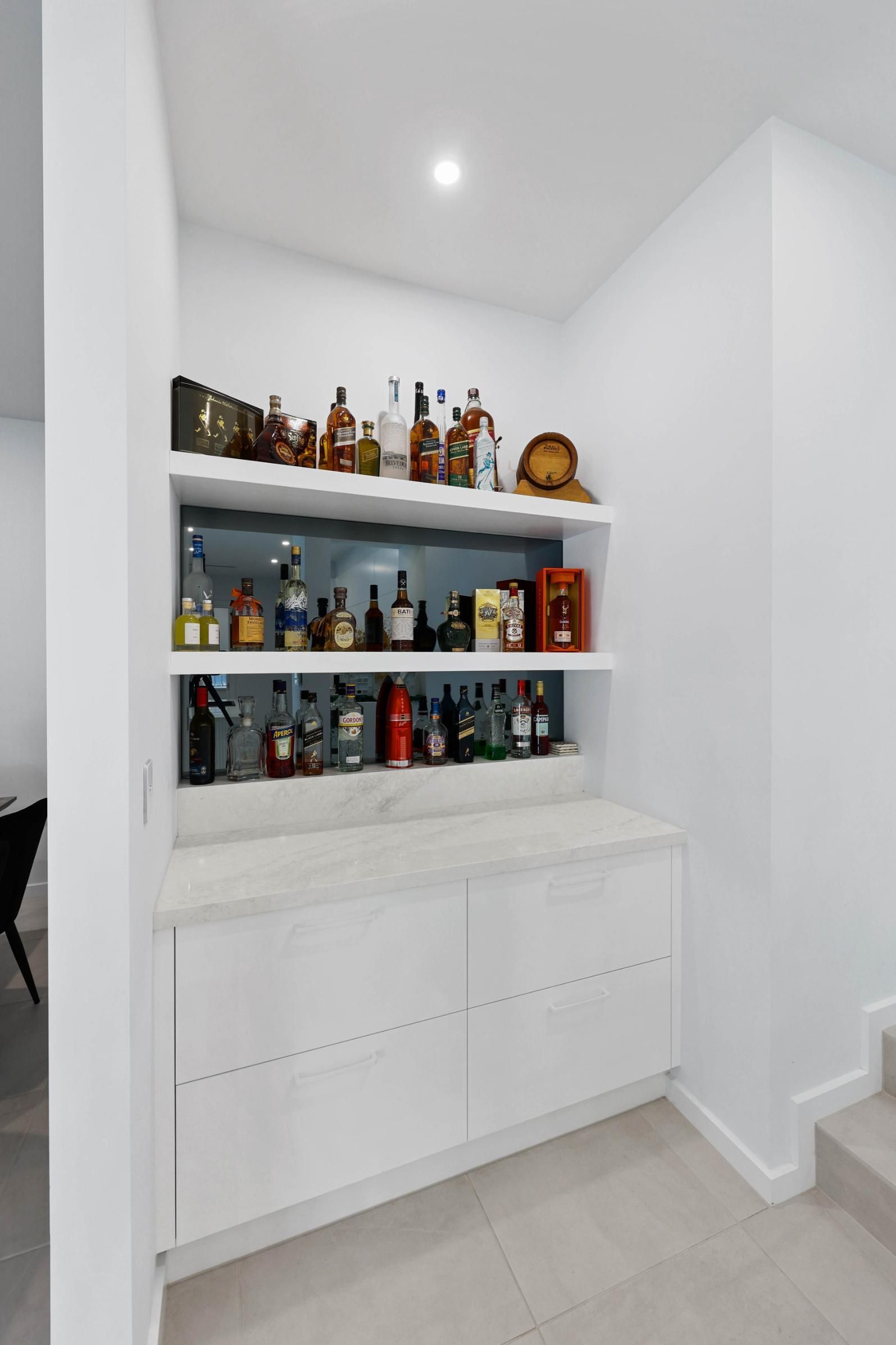 White Built-In Bar with Shelves Holding Bottles, Beneath a Marble Countertop and Cabinets. Located in A Hallway — Above & Beyond Interiors Custom Joinery in Currans Hill, NSW