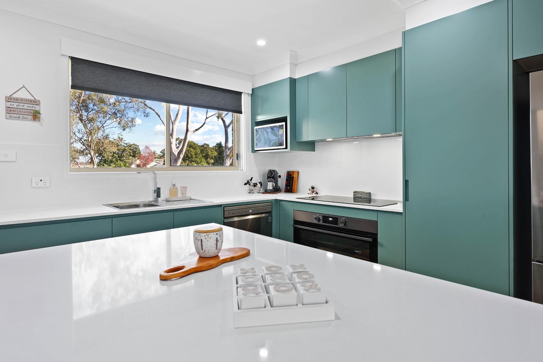 Modern Kitchen with White Countertops, Teal Cabinets, and A Window Overlooking Trees — Above & Beyond Interiors Custom Joinery in Bradbury, NSW