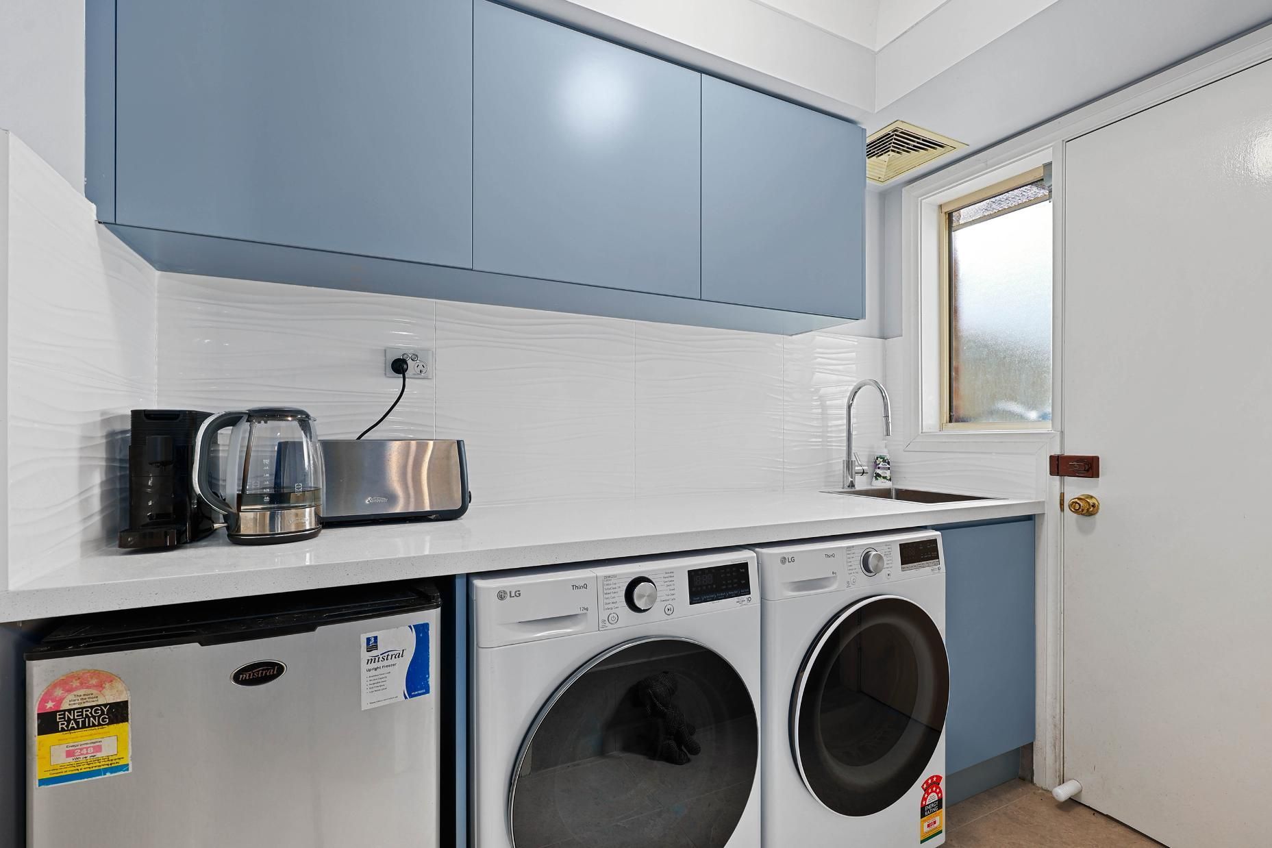 Laundry Room with A Blue Cabinet, White Countertop, and Appliances Including a Washer, Dryer, and Mini-Fridge — Above & Beyond Interiors Custom Joinery in Macquarie Fields, NSW