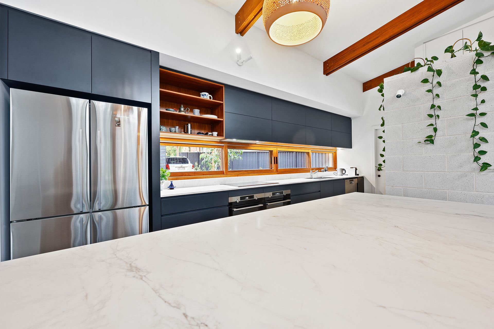 Modern kitchen with white countertop, dark blue cabinets, stainless steel fridge, and wooden accents — Above & Beyond Interiors Custom Joinery in Bellambi, NSW