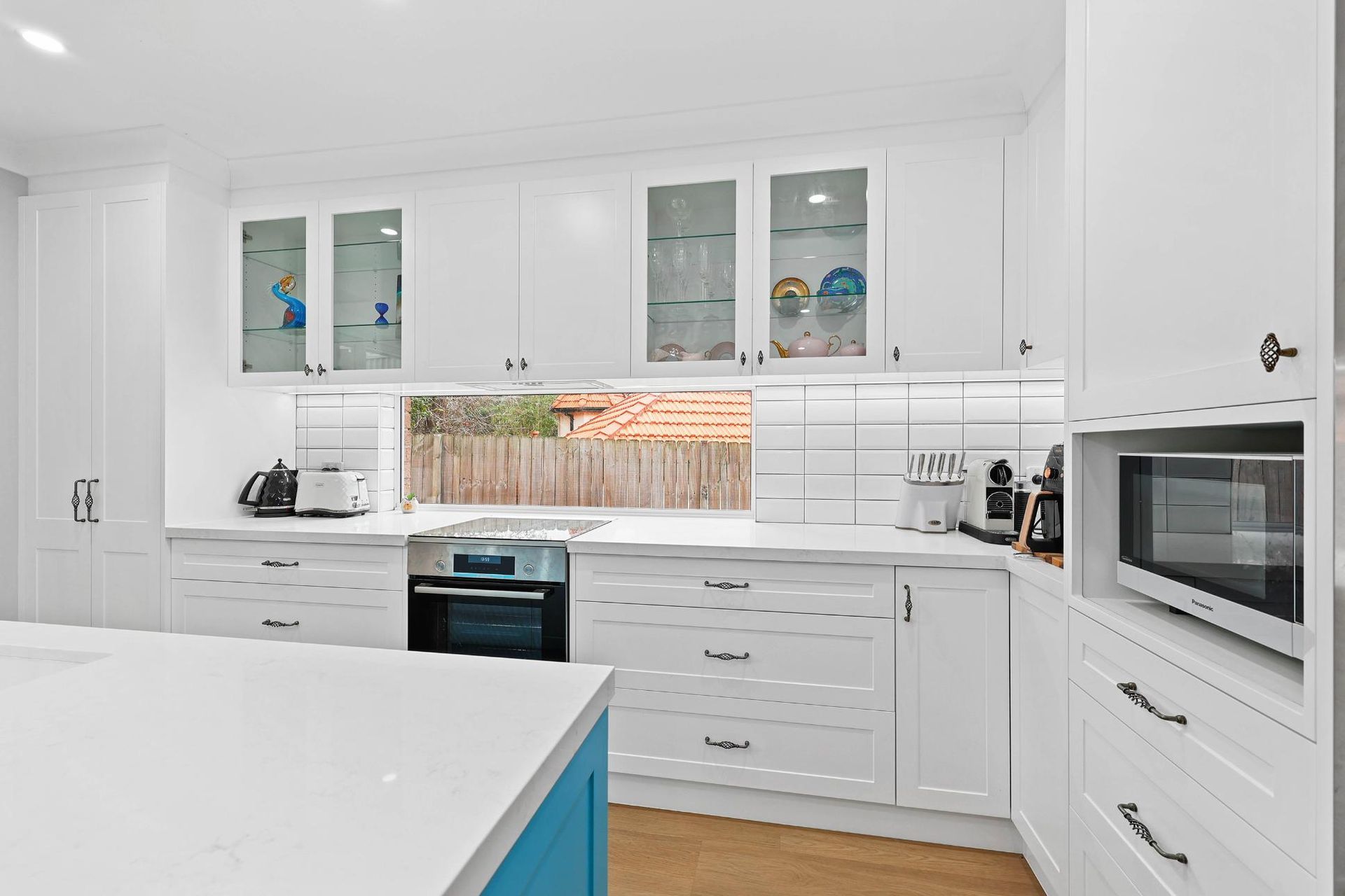 White Kitchen with Blue Island, Stainless Steel Appliances, and Glass-Front Cabinets — Above & Beyond Interiors Custom Joinery in Gladsville, NSW