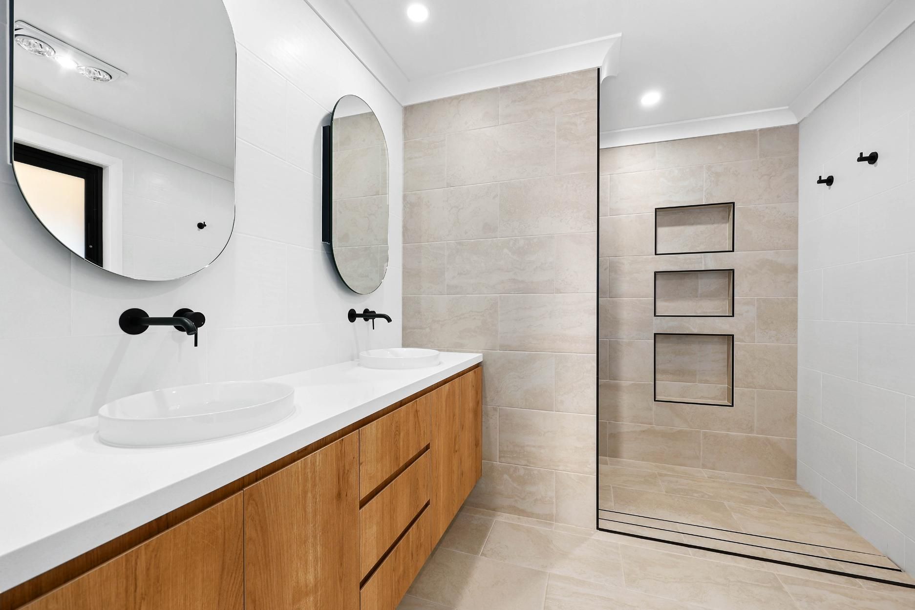 Modern Bathroom with Wood Vanity, Oval Mirrors, and Walk-In Shower with Tile and Recessed Shelves — Above & Beyond Interiors Custom Joinery in Abbortsbury, NSW