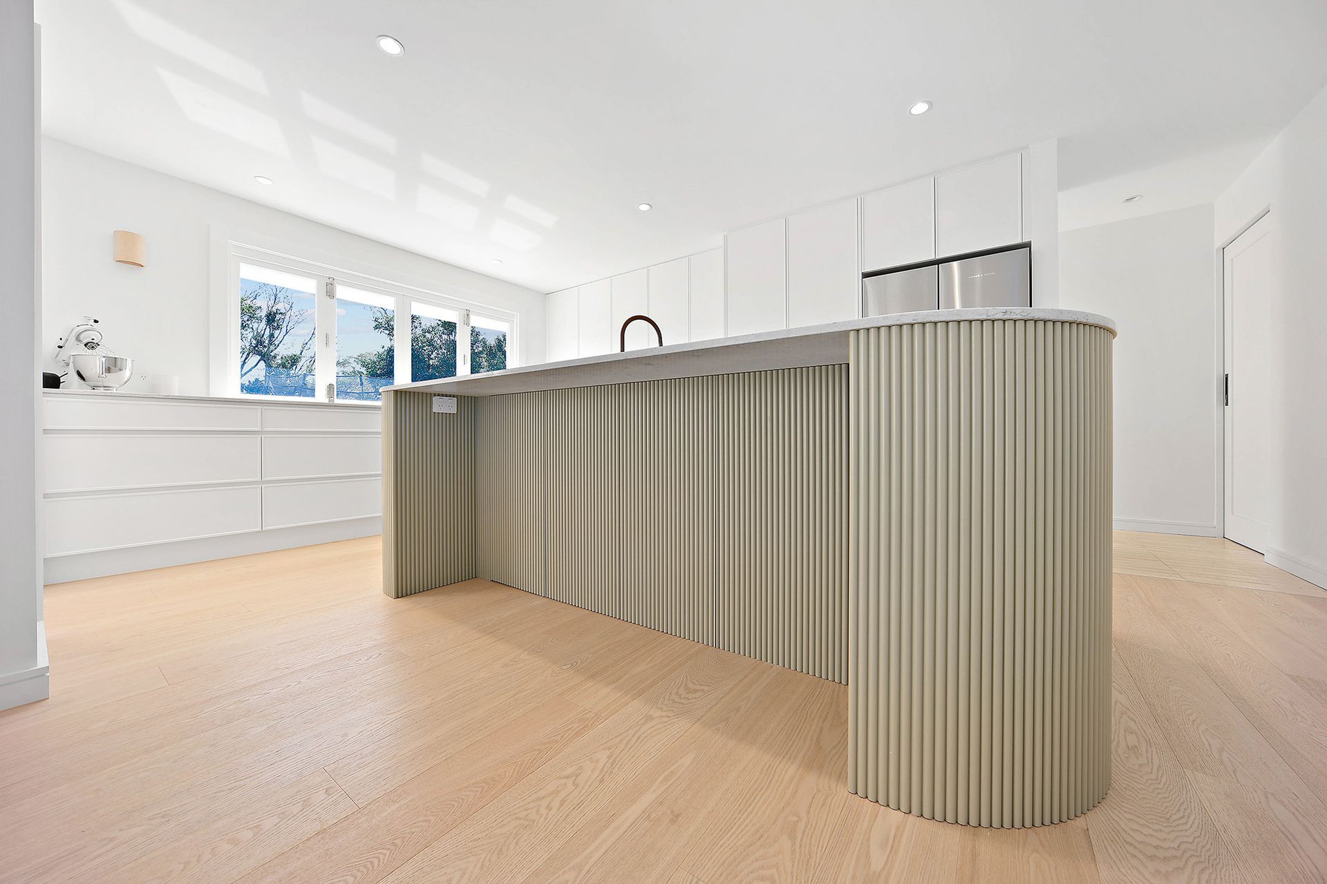 Modern white kitchen with light wood floors. Island has fluted, light green front — Above & Beyond Interiors Custom Joinery in Bellambi, NSW