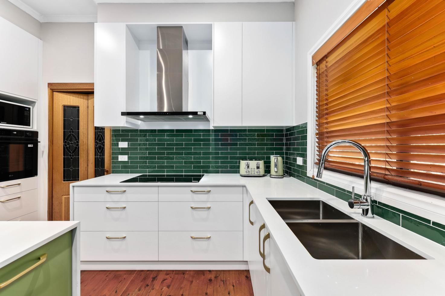 Modern Kitchen with White Cabinets, Green Backsplash, and Stainless Steel Hood; Wooden Blinds — Above & Beyond Interiors Custom Joinery in Minto, NSW