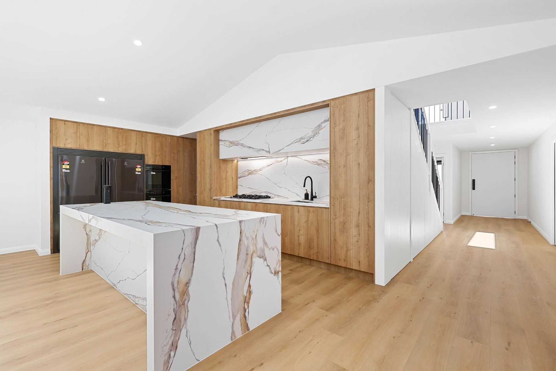 Modern Kitchen with Marble Island, Wooden Cabinets, Black Appliances, and Light Wood Floors — Above & Beyond Interiors Custom Joinery in Abbortsbury, NSW