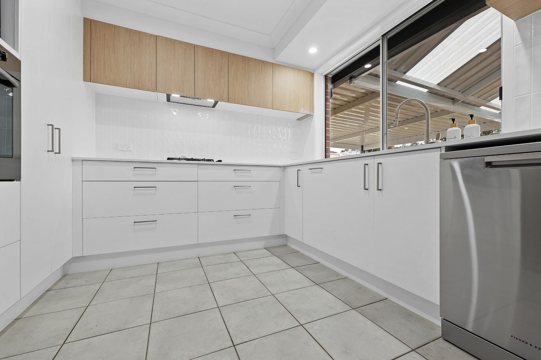 White Modern Kitchen with Wood Cabinets, Stainless Steel Appliances, and A Large Window — Above & Beyond Interiors Custom Joinery in Currans Hill, NSW