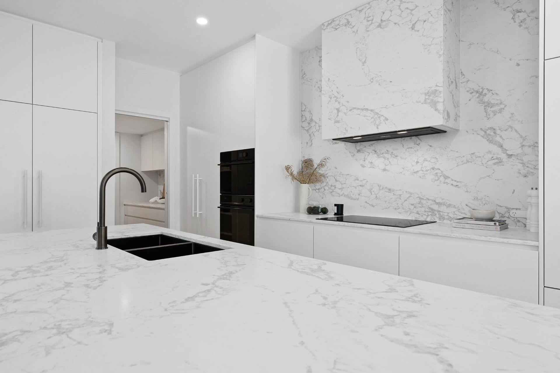 Modern White Kitchen with Marble Countertops, Sink, and Stovetop. Black Faucet and Hood — Above & Beyond Interiors Custom Joinery in Thirroul, NSW