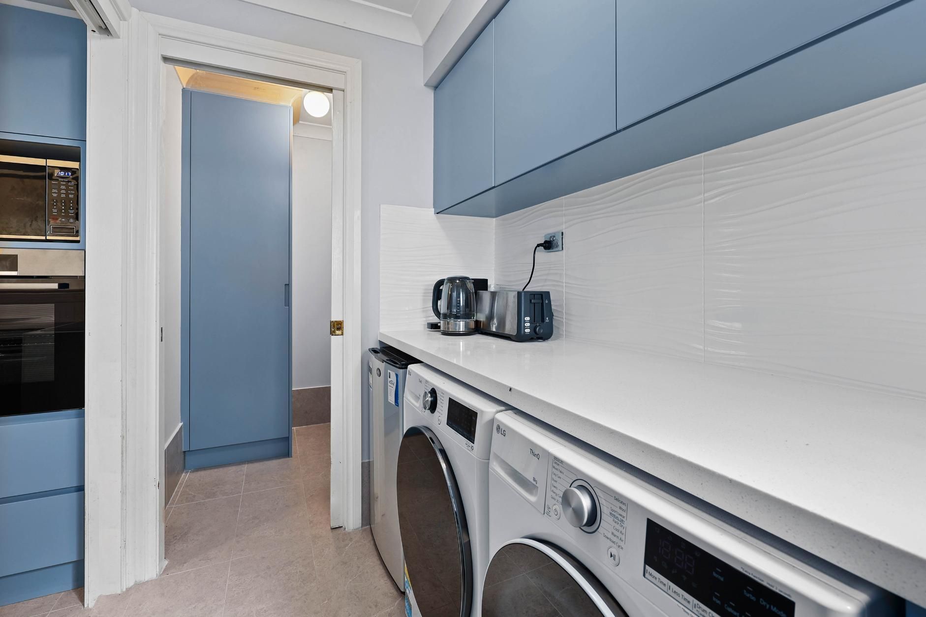 A Blue and White Laundry Room with A Washing Machine, Dryer, and Cabinets — Above & Beyond Interiors Custom Joinery in Macquarie Fields, NSW