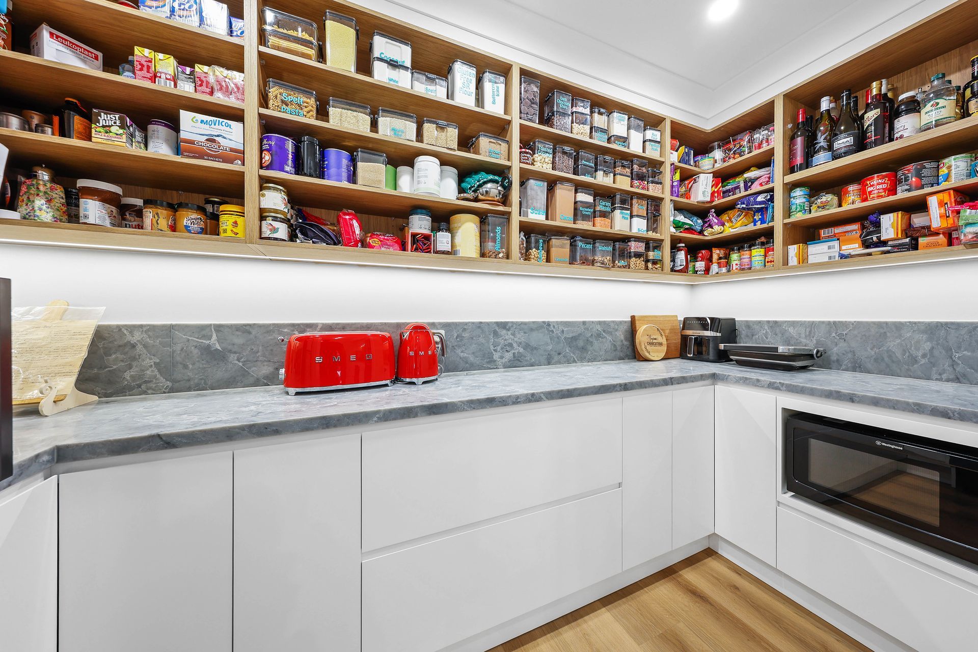 Modern pantry with white cabinets, stone countertop, and shelves filled with food — Above & Beyond Interiors Custom Joinery in Bellambi, NSW