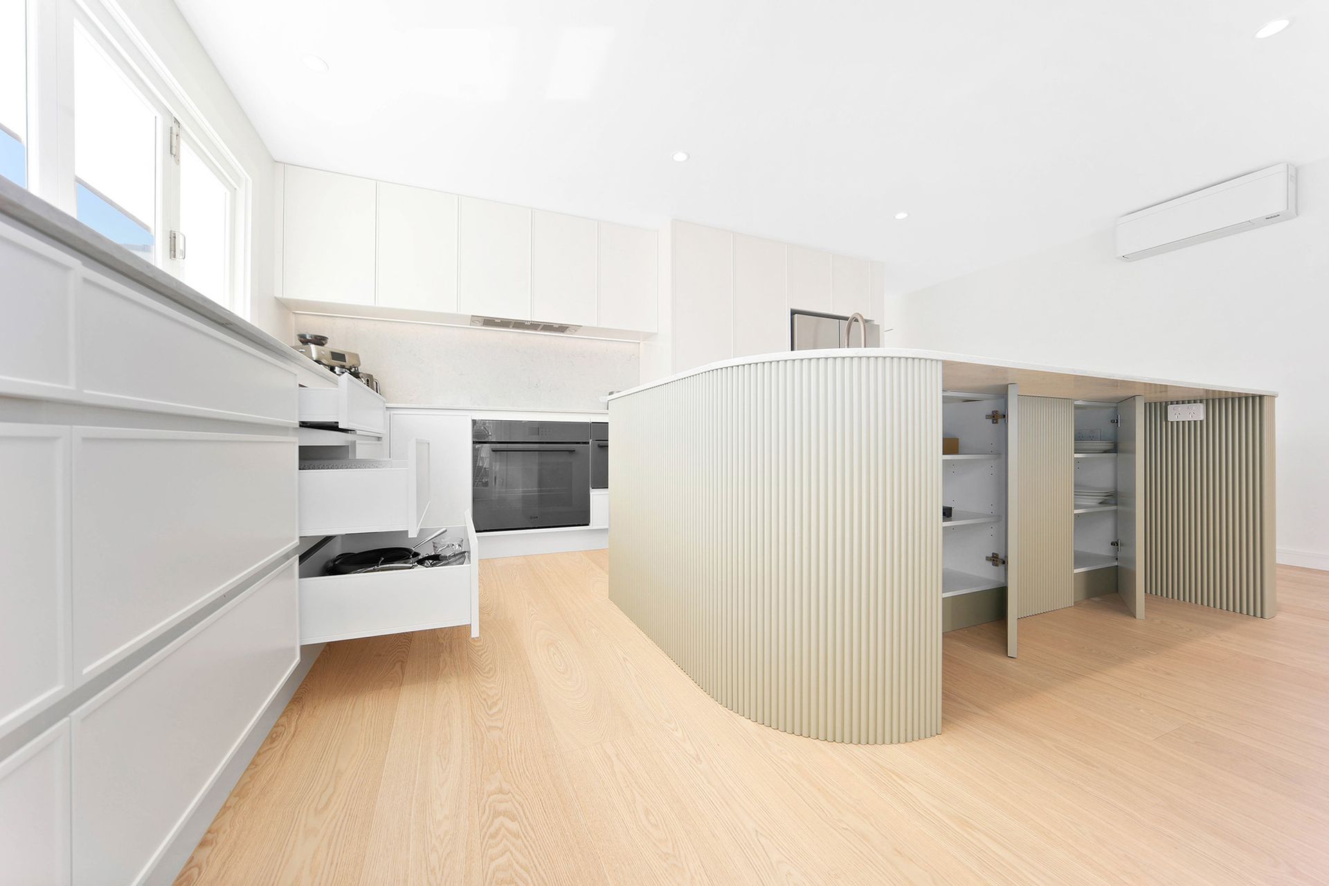 Modern white kitchen with curved island and light wood floors — Above & Beyond Interiors Custom Joinery in Bellambi, NSW