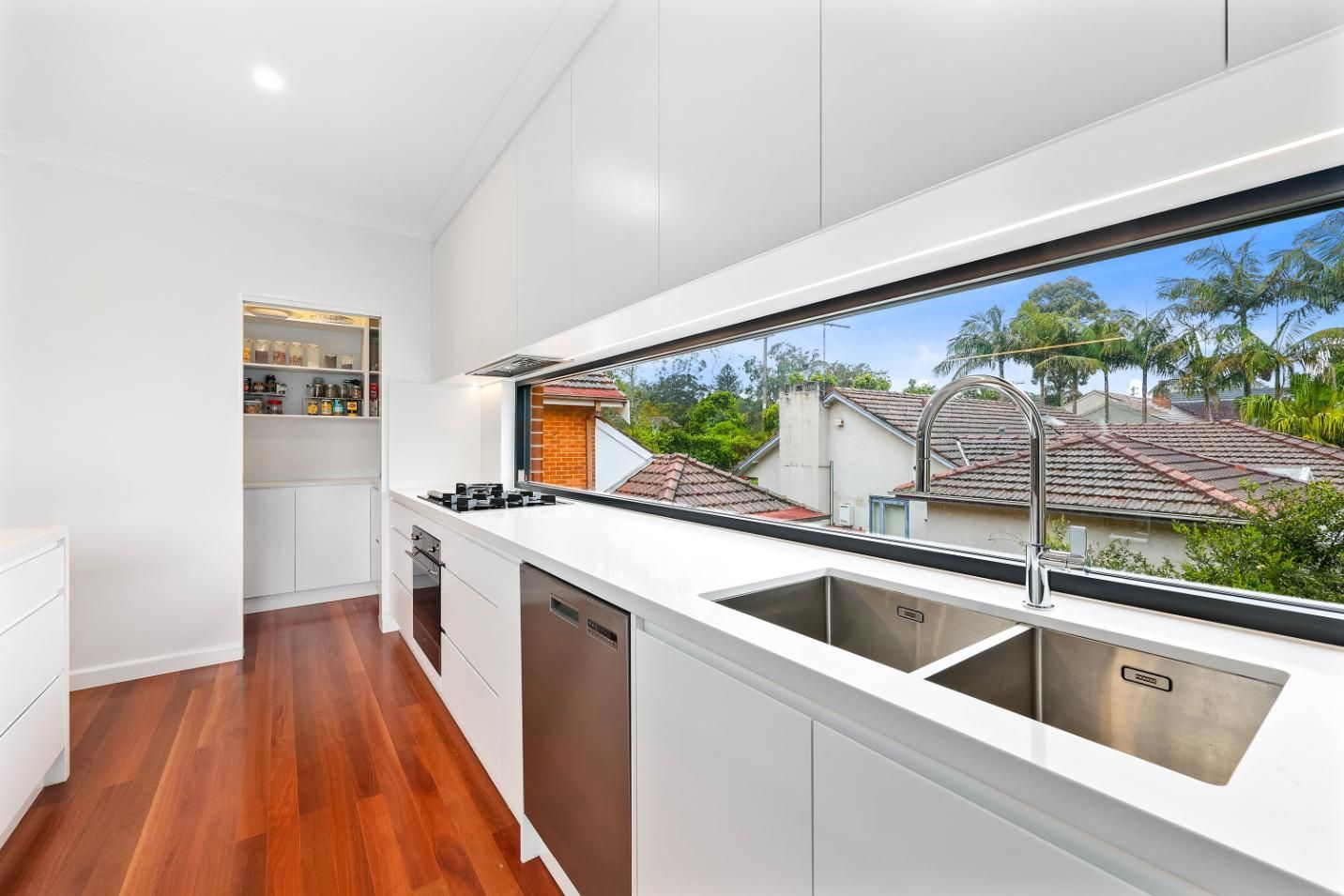 Modern White Kitchen with Large Window Overlooking Rooftops and Trees — Above & Beyond Interiors Custom Joinery in Killara, NSW