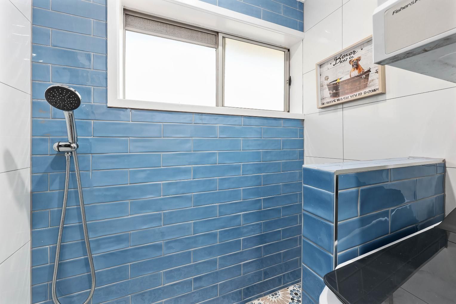 Blue Tiled Shower Stall with A Window, a Showerhead, and A Vintage Poster on The Wall — Above & Beyond Interiors Custom Joinery in Bradbury, NSW