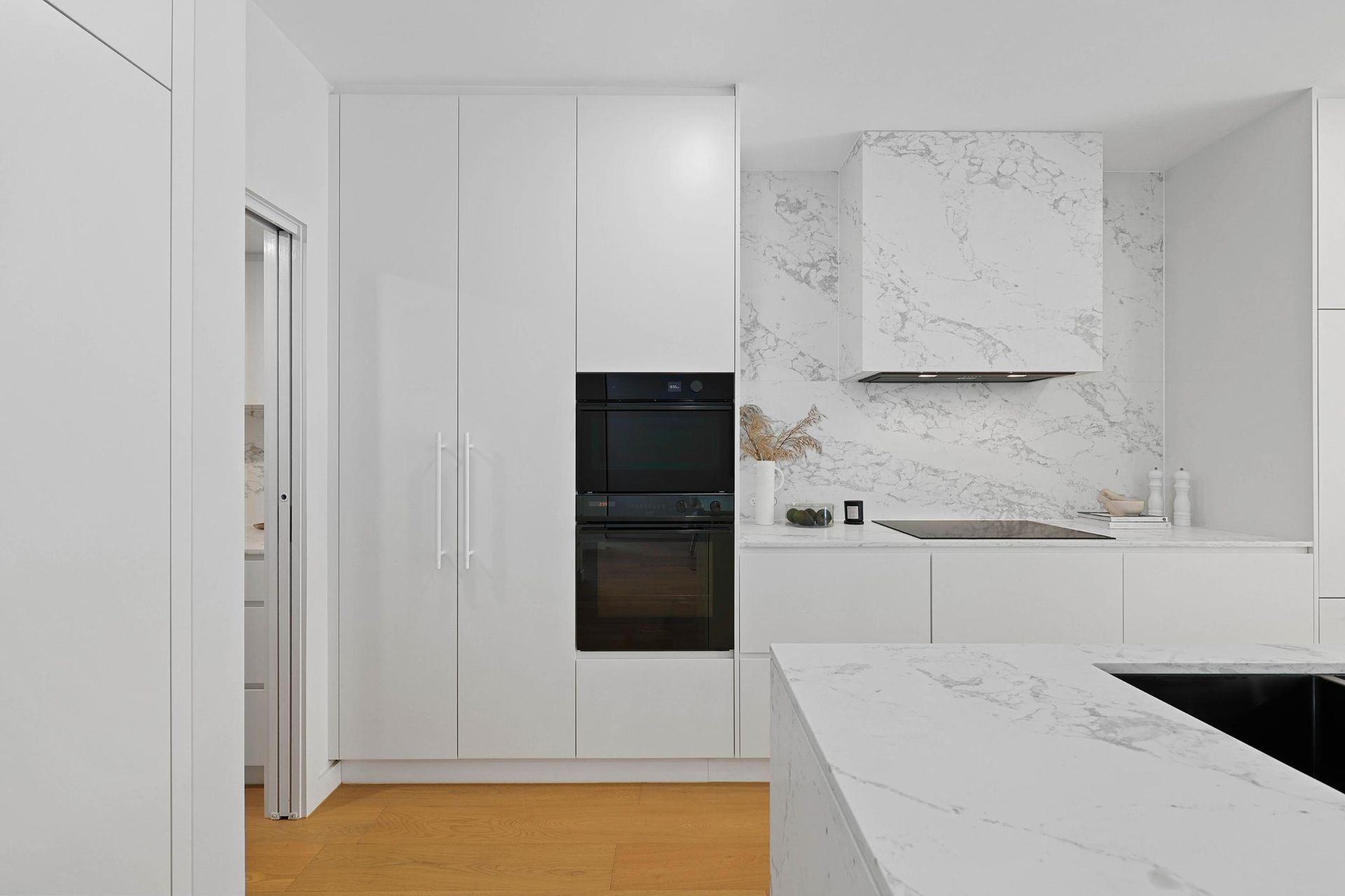 Modern White Kitchen with Marble Backsplash, Built-In Oven, and Island with A Dark Sink — Above & Beyond Interiors Custom Joinery in Thirroul, NSW
