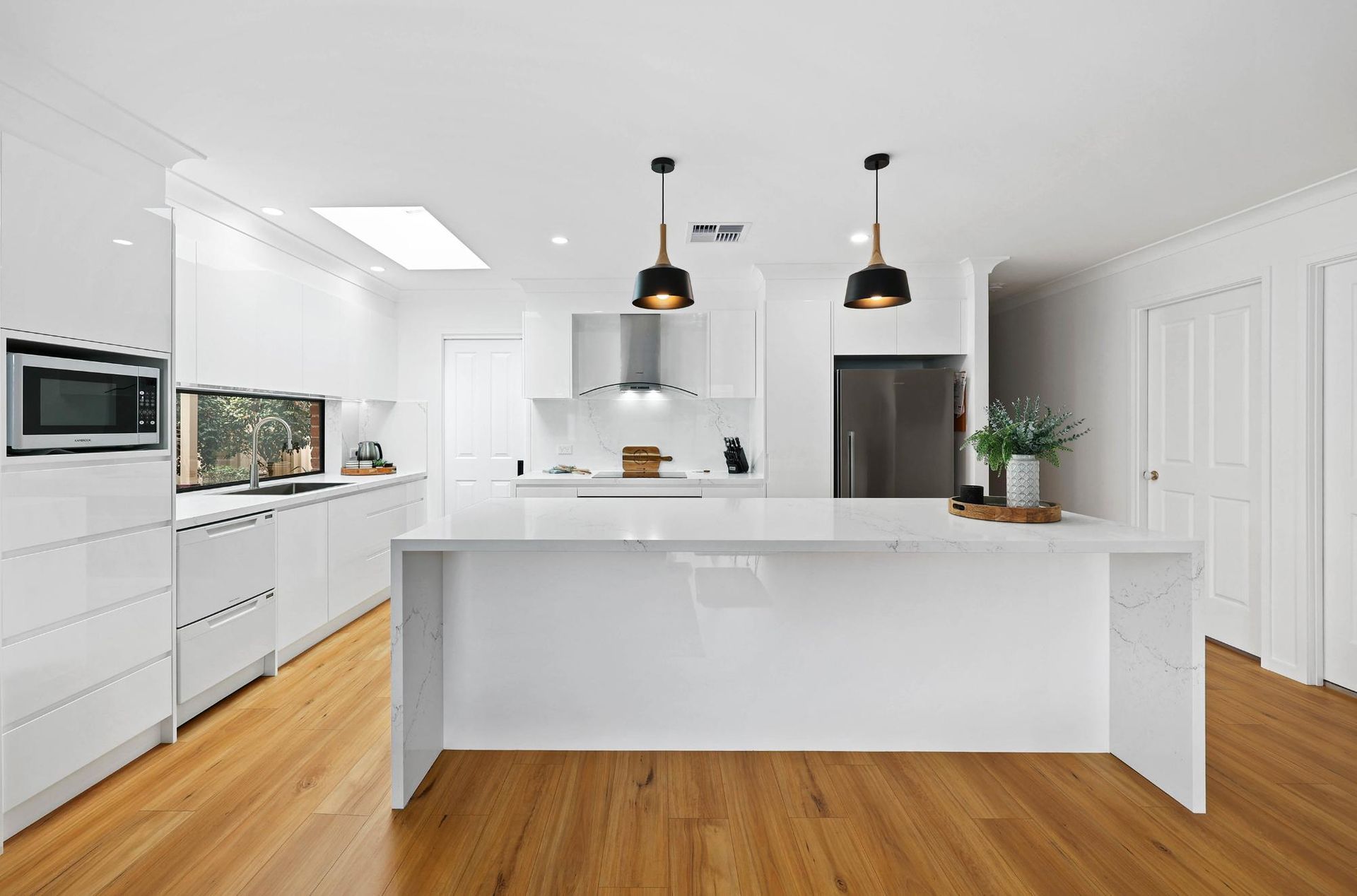 Modern White Kitchen with Island, Wooden Floors, and Black Pendant Lights — Above & Beyond Interiors Custom Joinery in Wattle Grove, NSW