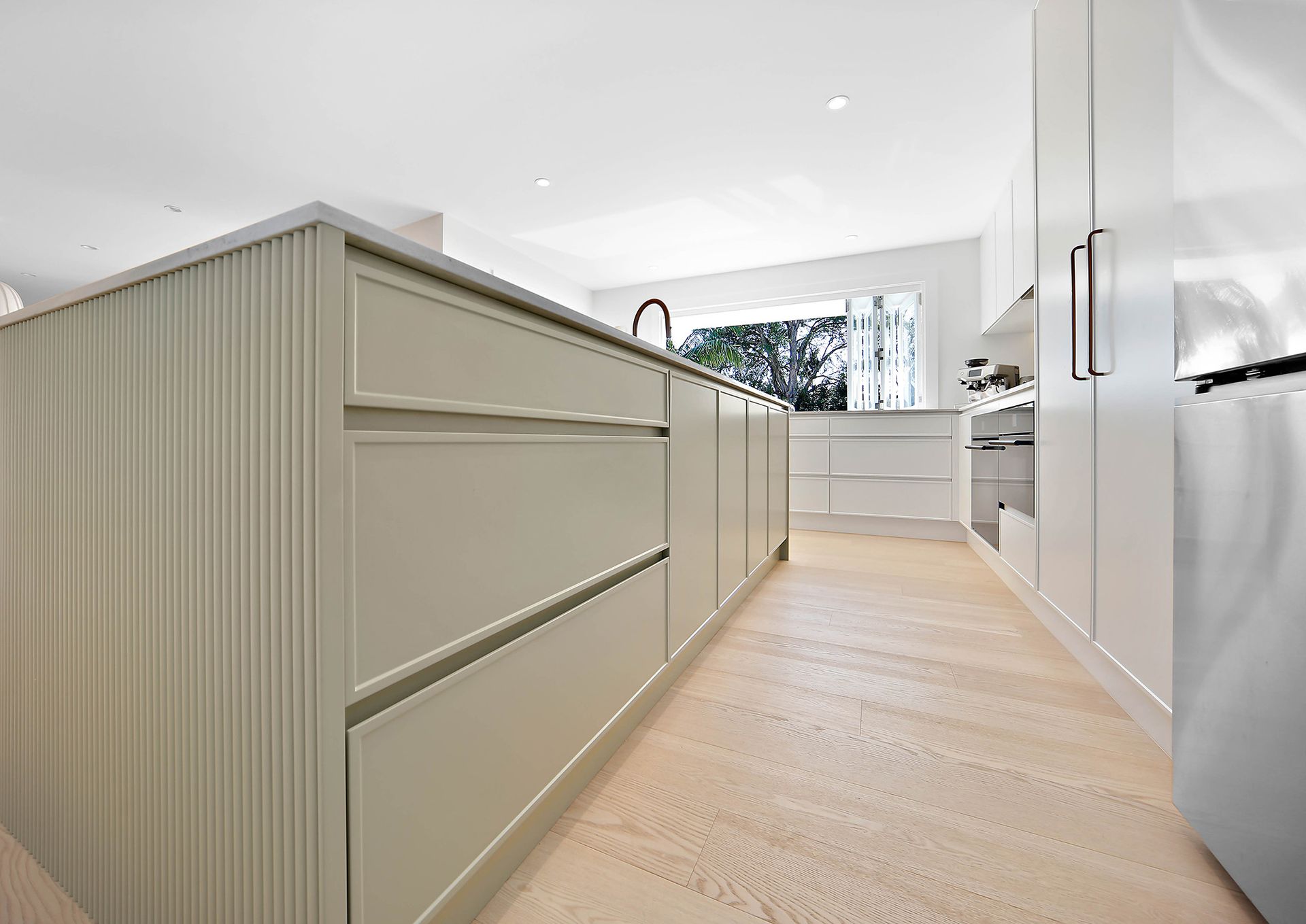 Modern kitchen with a light green island, light wood floors, and white cabinets — Above & Beyond Interiors Custom Joinery in Bellambi, NSW