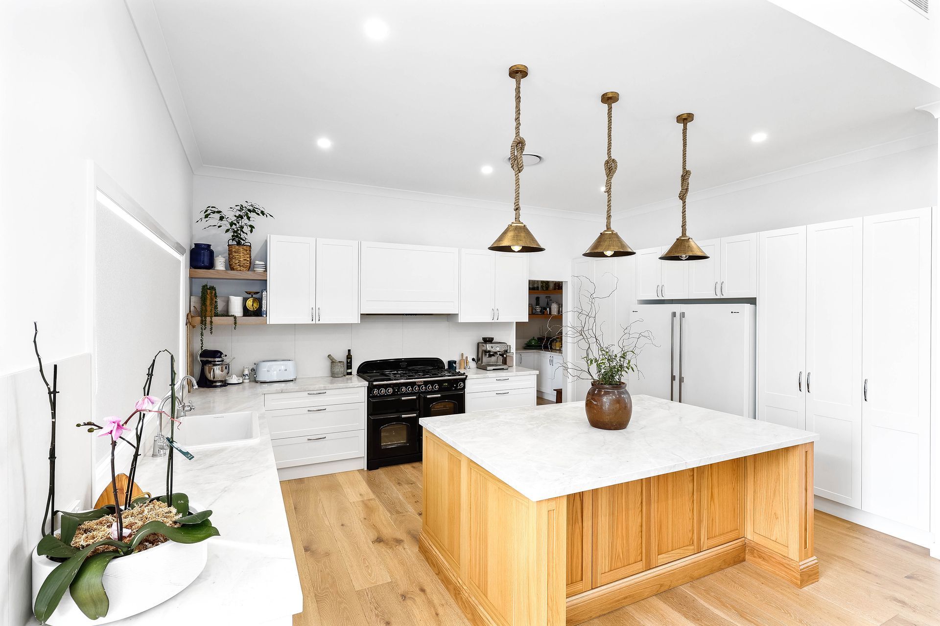 Modern kitchen with white cabinets, wooden island, pendant lights, and hardwood floor — Above & Beyond Interiors in Wollongong, NSW