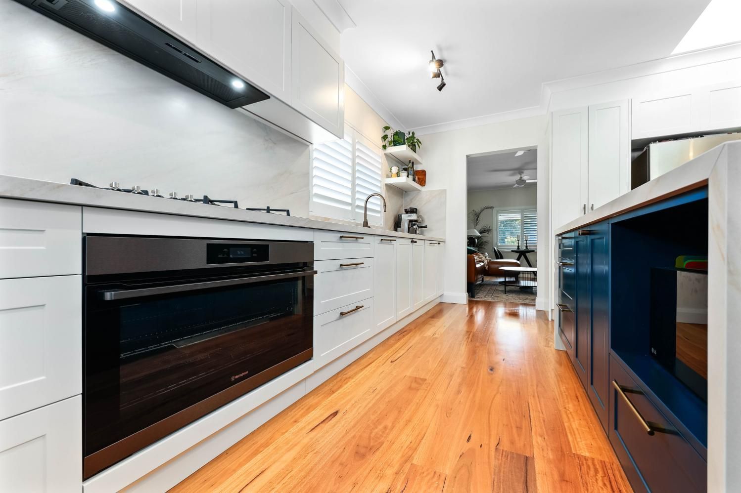 Modern Kitchen with White Cabinets, Dark Oven, and Blue Island; Wood Floors and Doorway to Other Room — Above & Beyond Interiors Custom Joinery in Bellambi, NSW