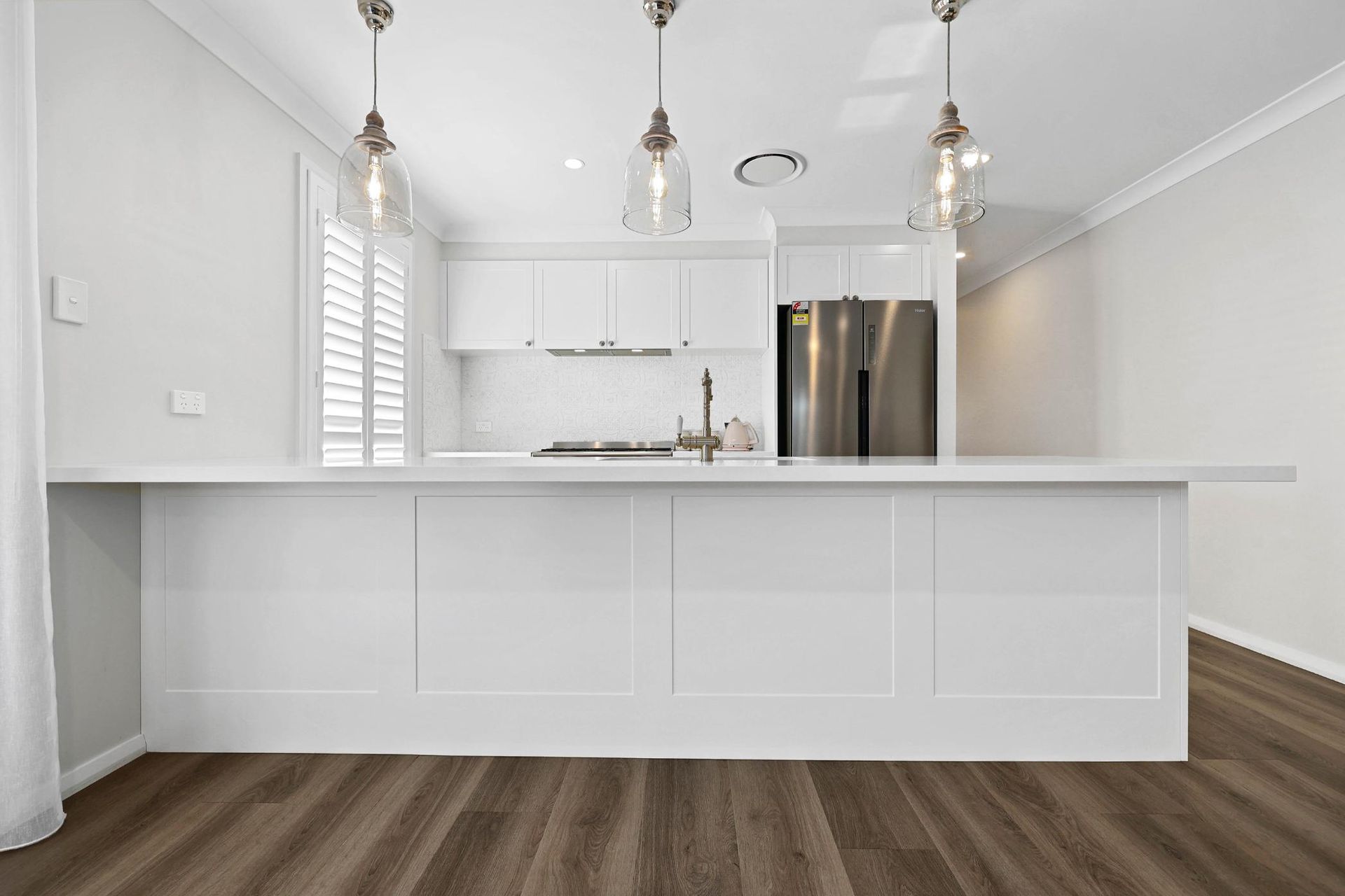 Bright White Kitchen with Large Island, Pendant Lights, and Stainless Steel Appliances — Above & Beyond Interiors Custom Joinery in Thirlmere, NSW