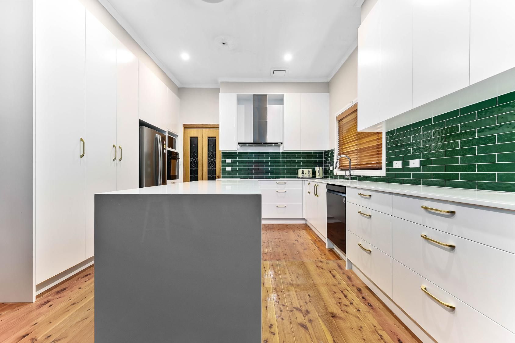 Modern Kitchen with White Cabinets, Green Backsplash, Wooden Floors, and A Grey Island — Above & Beyond Interiors Custom Joinery in Minto, NSW