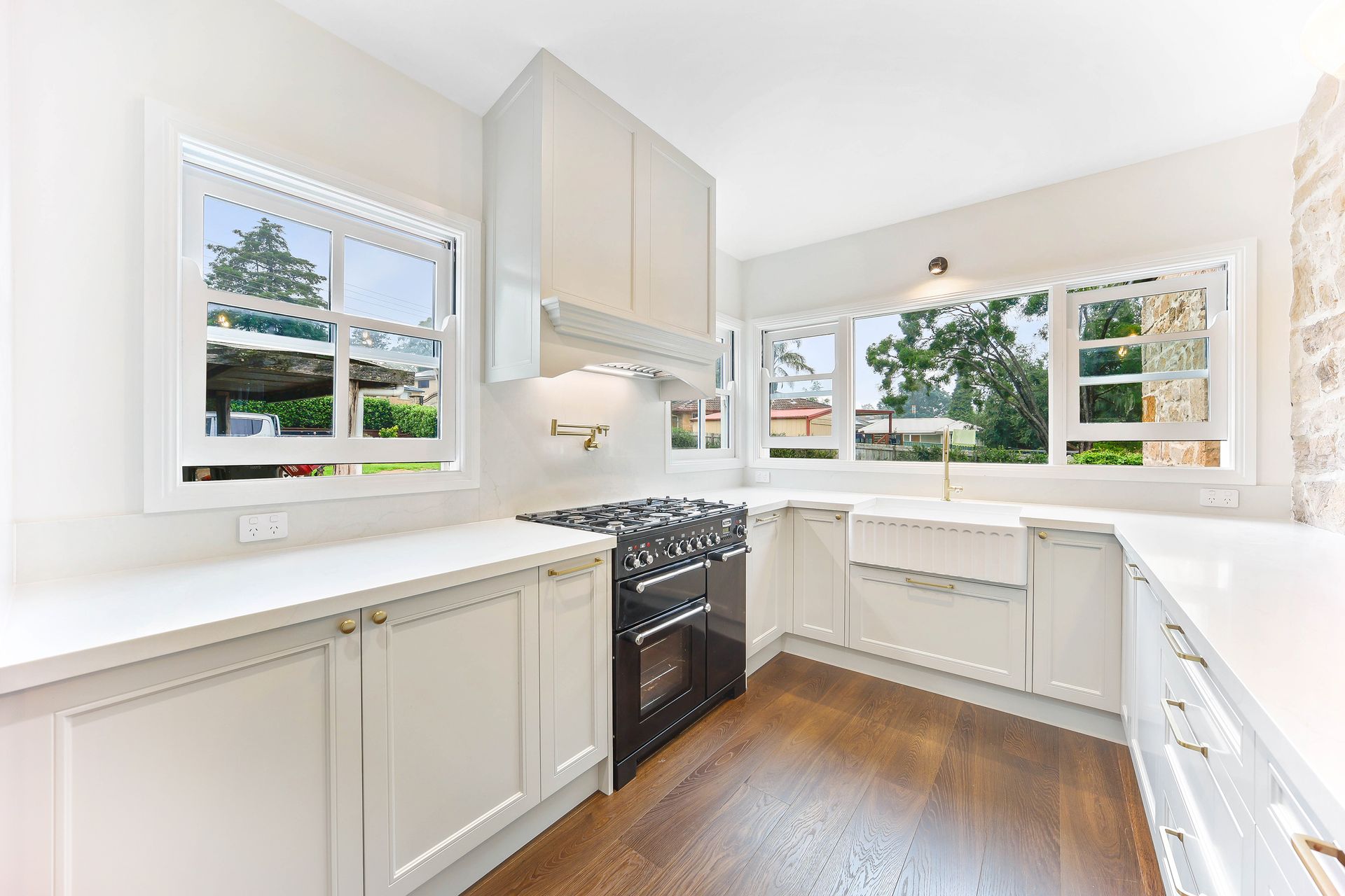Bright white kitchen with dark stovetop, windows, and hardwood floor — Above & Beyond Interiors Custom Joinery in Bradbury, NSW