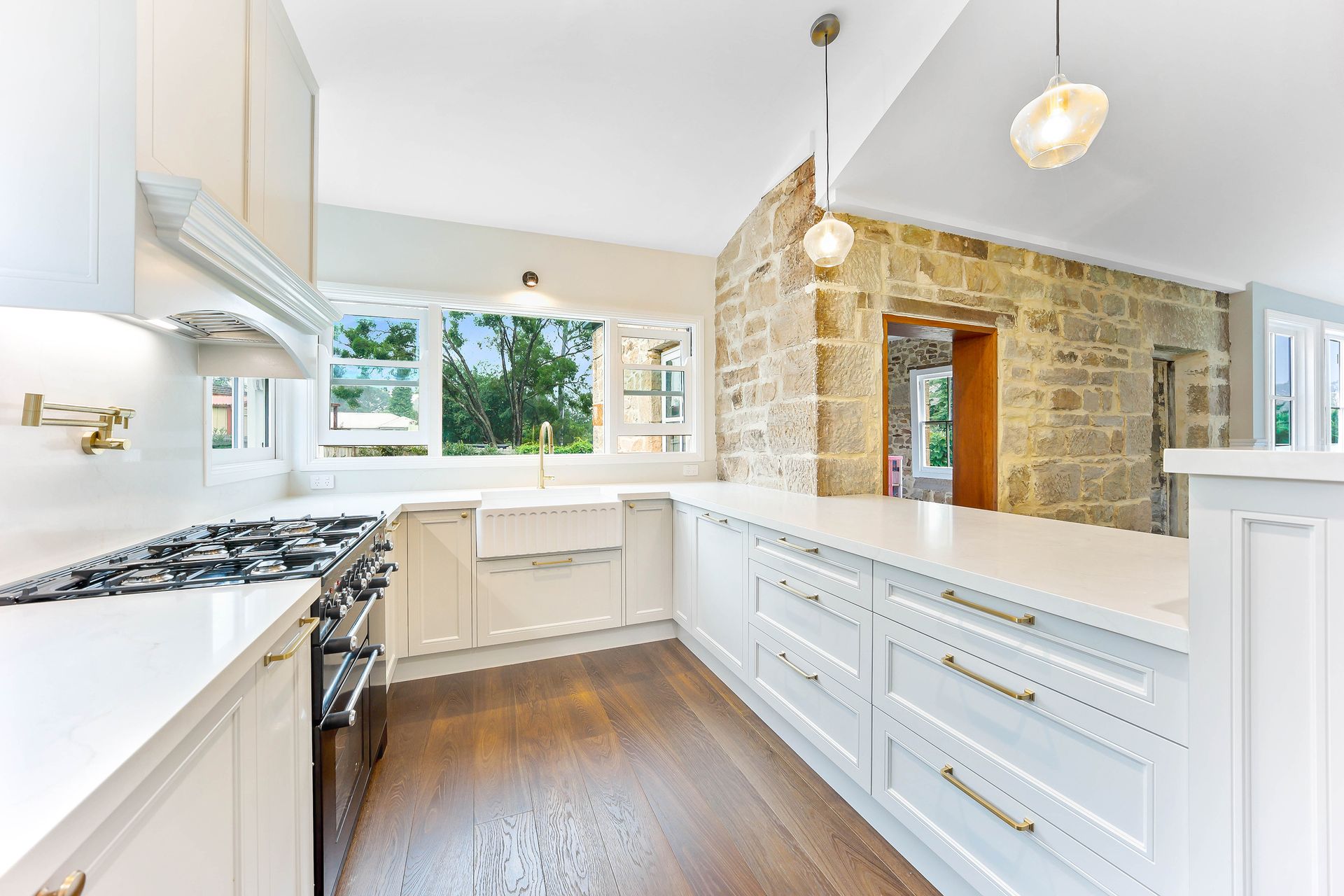 White kitchen with stone wall, cabinets, countertops, and stainless steel stove — Above & Beyond Interiors Custom Joinery in Bradbury, NSW