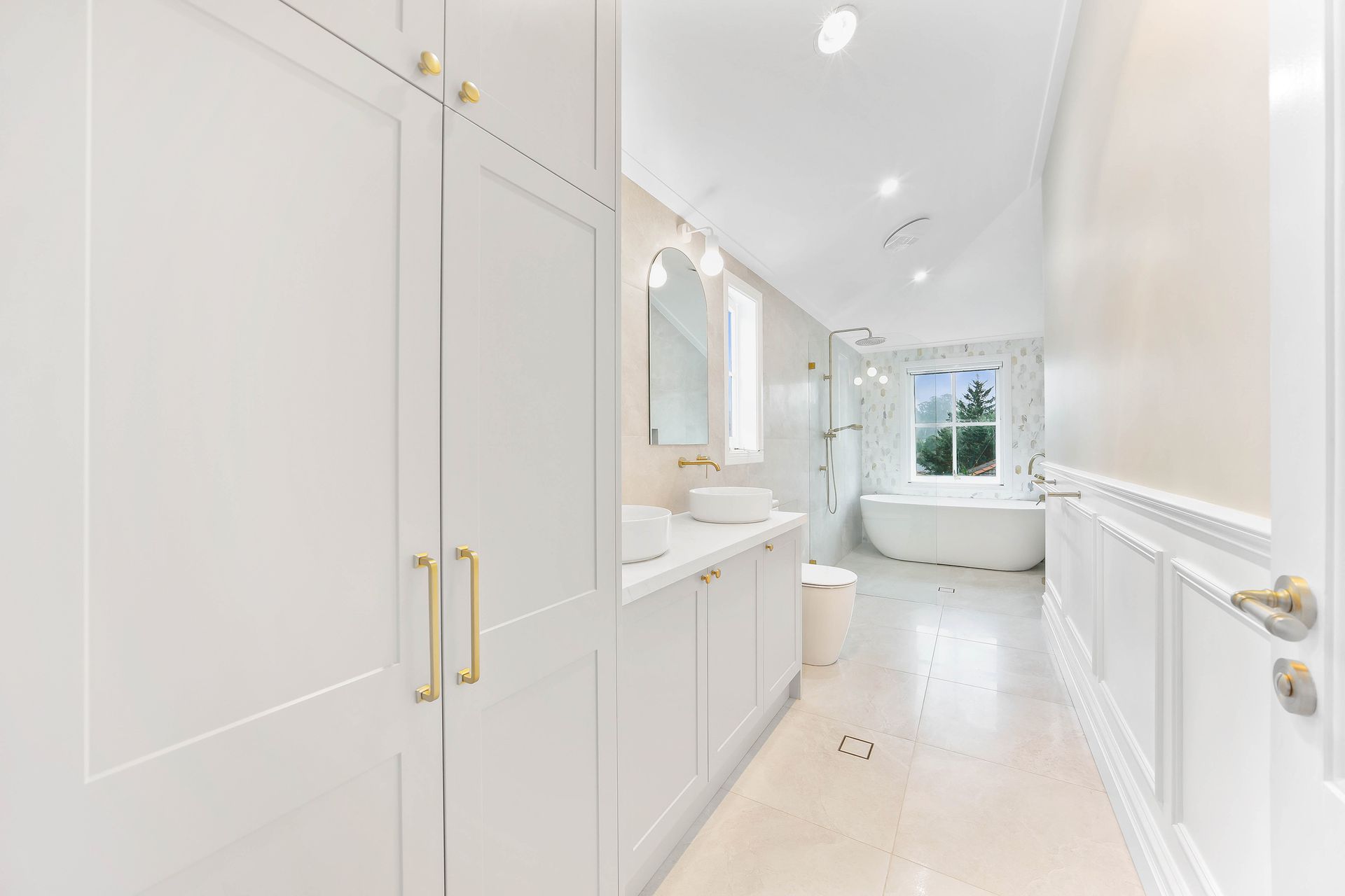 White bathroom with tall cabinets, vanity, and a soaking tub near a window — Above & Beyond Interiors Custom Joinery in Bradbury, NSW