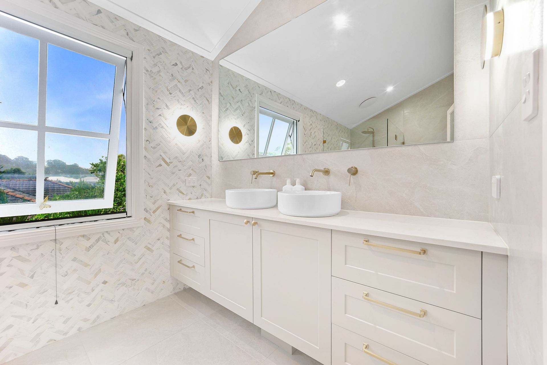 Bright white bathroom with double sinks, a large mirror, and window overlooking a landscape — Above & Beyond Interiors Custom Joinery in Bradbury, NSW