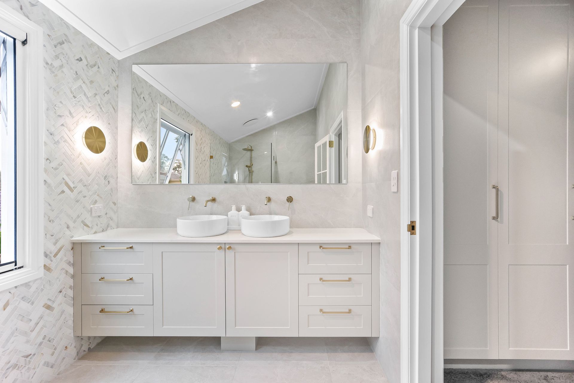 White bathroom with double sinks, gold fixtures, and large mirror — Above & Beyond Interiors Custom Joinery in Bellambi, NSW
