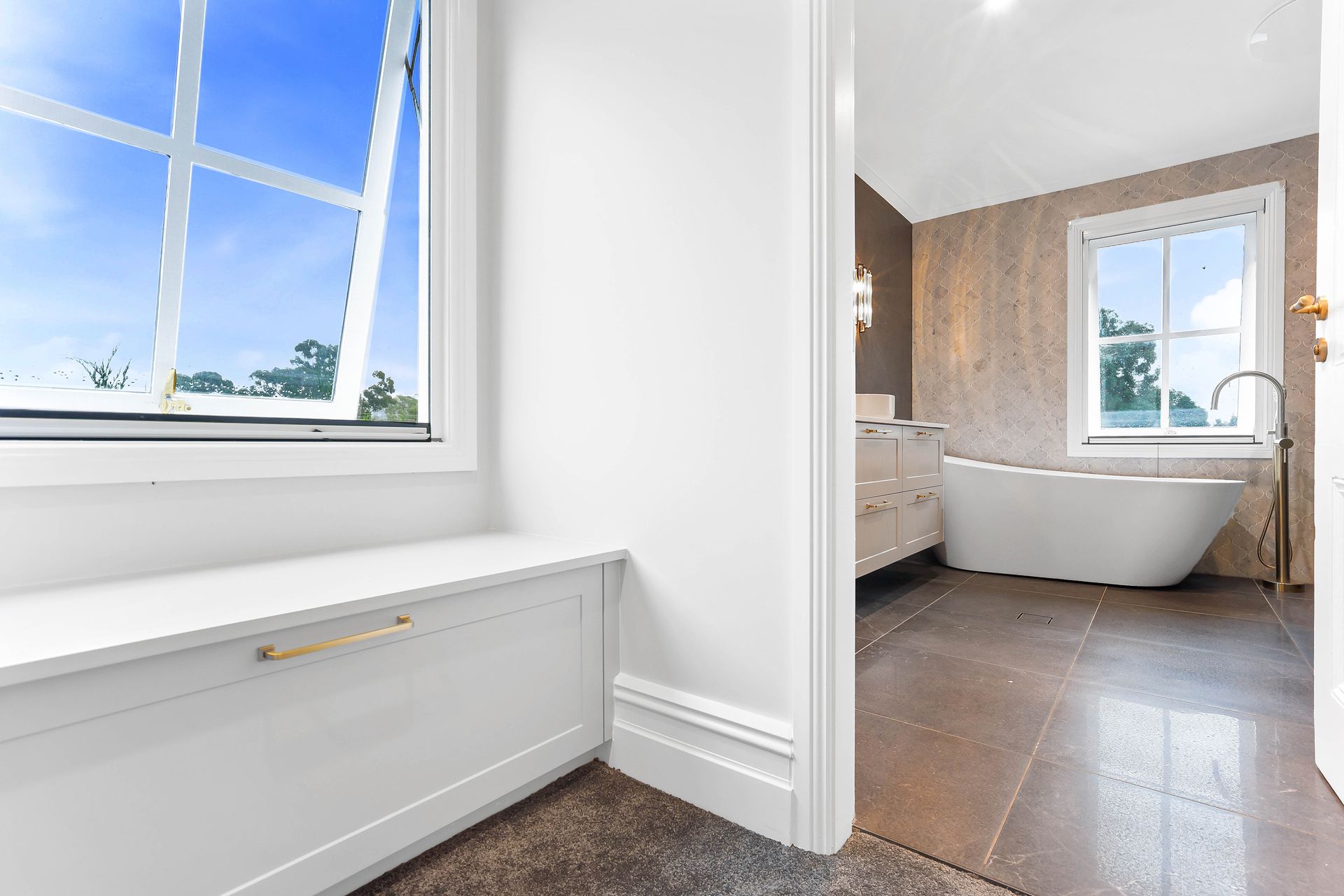 A modern bathroom with a freestanding tub, window, and a built-in bench with a view to the outside — Above & Beyond Interiors Custom Joinery in Bradbury, NSW