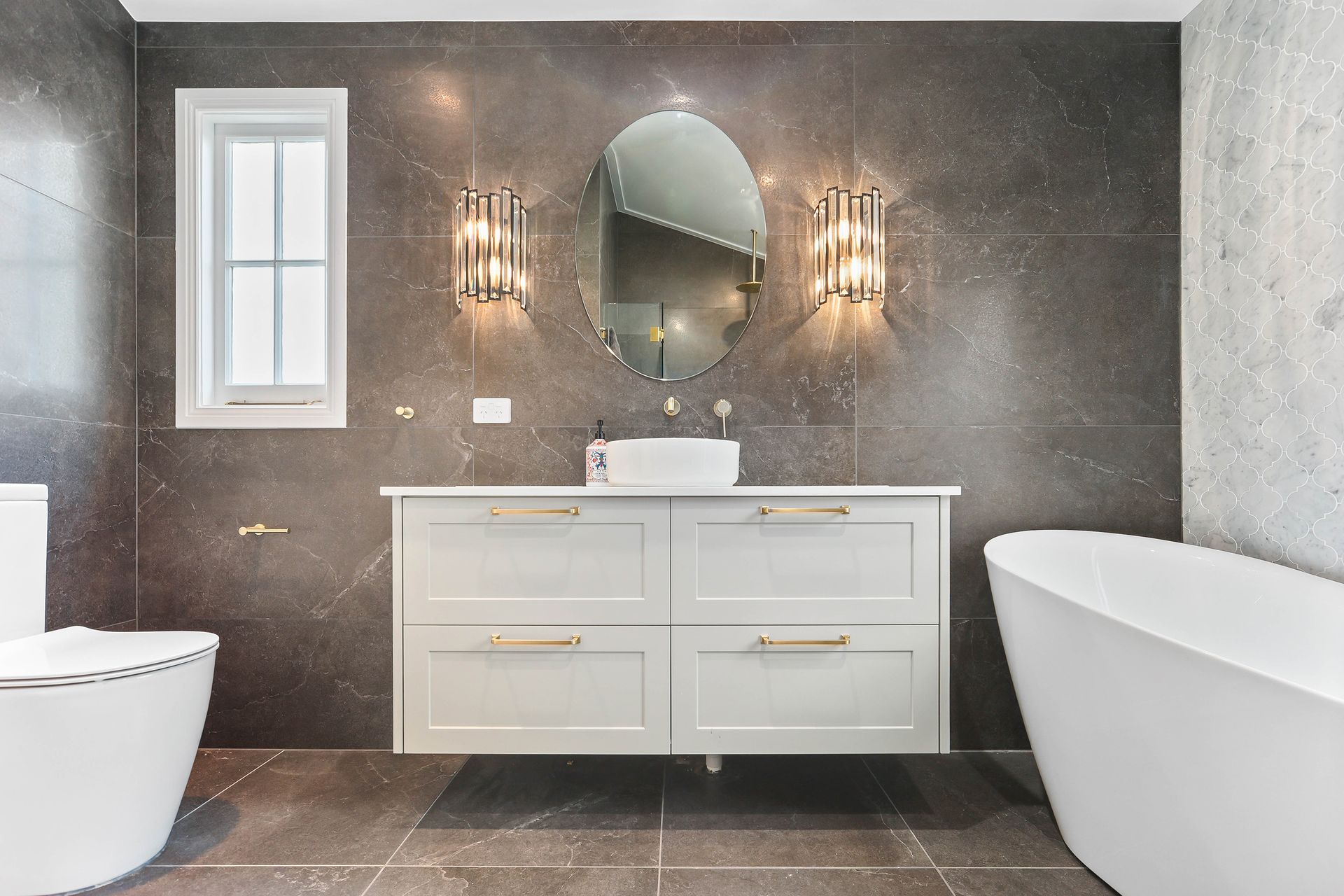 Modern bathroom with grey tile walls, floating vanity, oval mirror, and freestanding tub — Above & Beyond Interiors Custom Joinery in Bradbury, NSW