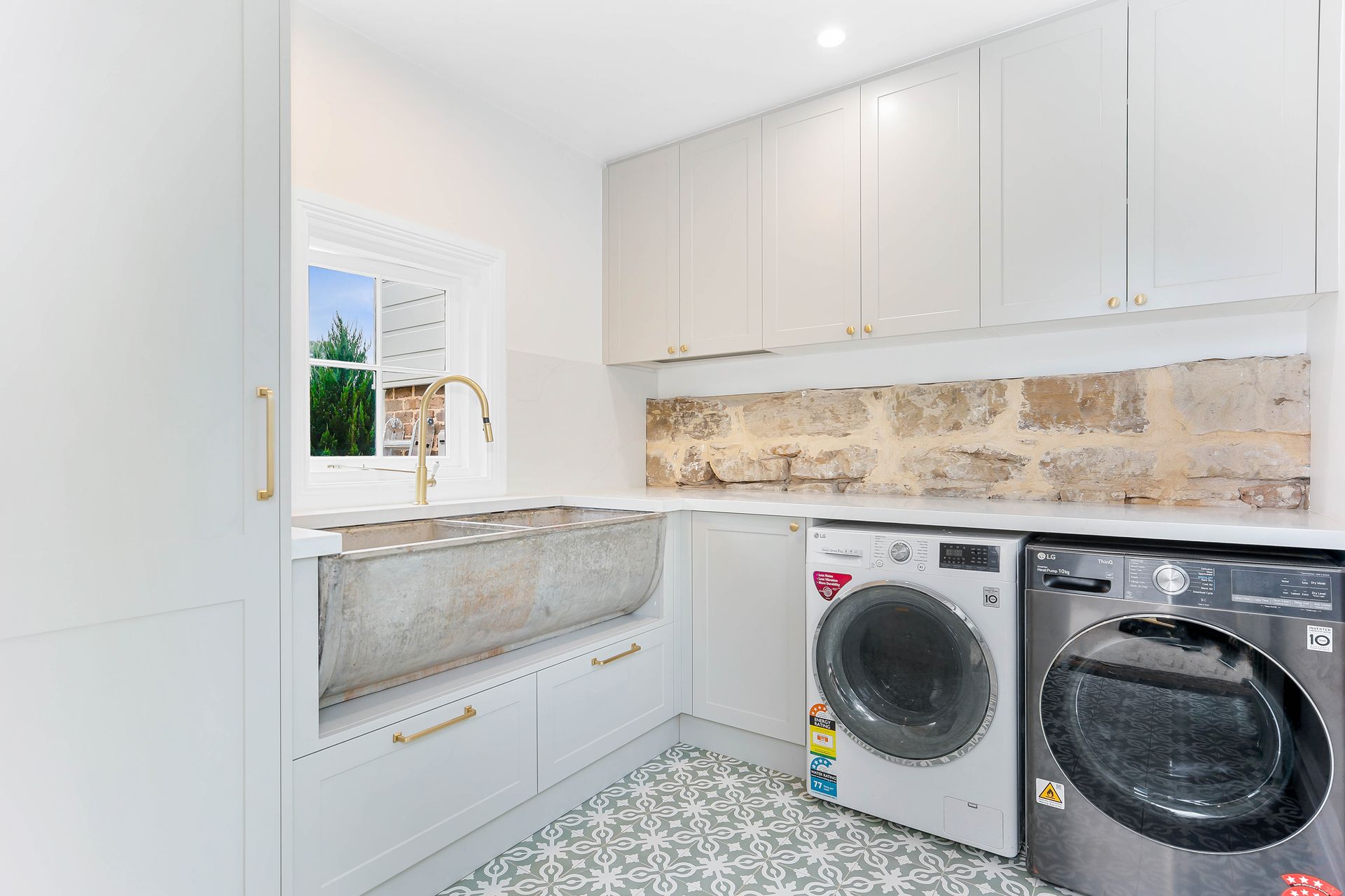 Laundry room with white cabinets, stone backsplash, silver sink, and grey appliances — Above & Beyond Interiors Custom Joinery in Bradbury, NSW