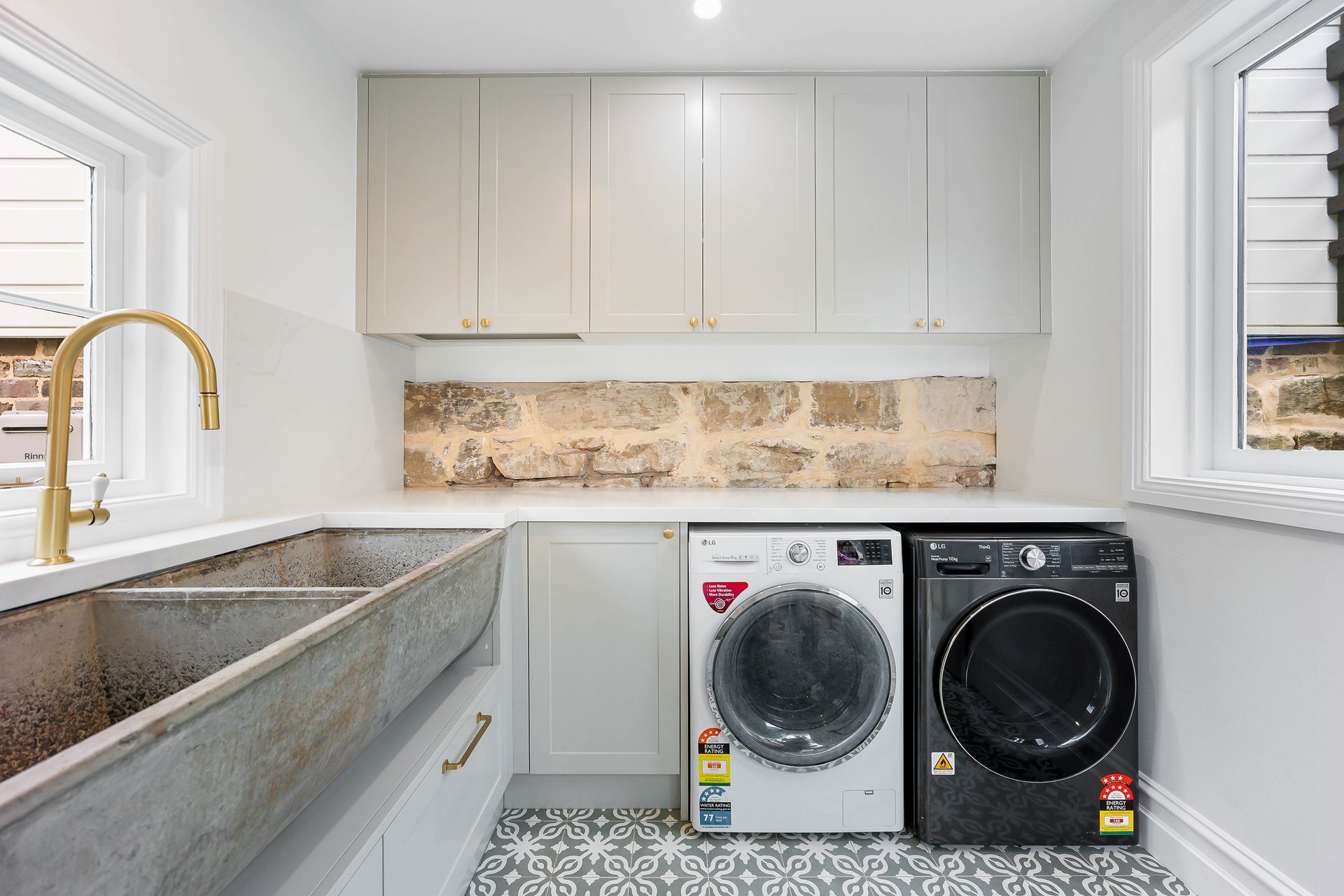 Laundry room with light grey cabinets, stone backsplash, two washing machines, and a concrete sink — Above & Beyond Interiors Custom Joinery in Bradbury, NSW