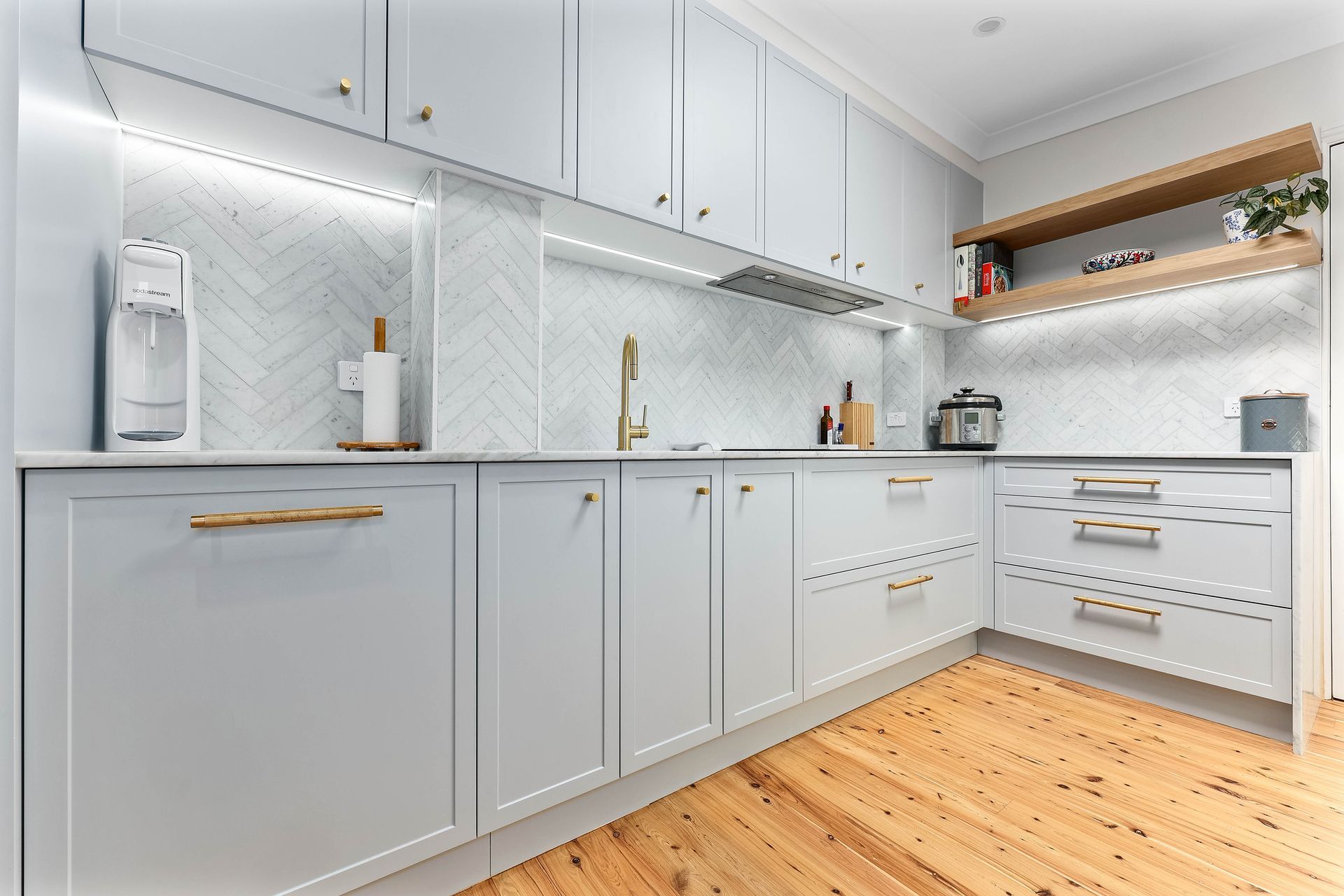 Light blue kitchen with herringbone backsplash, wooden shelves, and gold hardware — Above & Beyond Interiors in Smeaton Grange, NSW