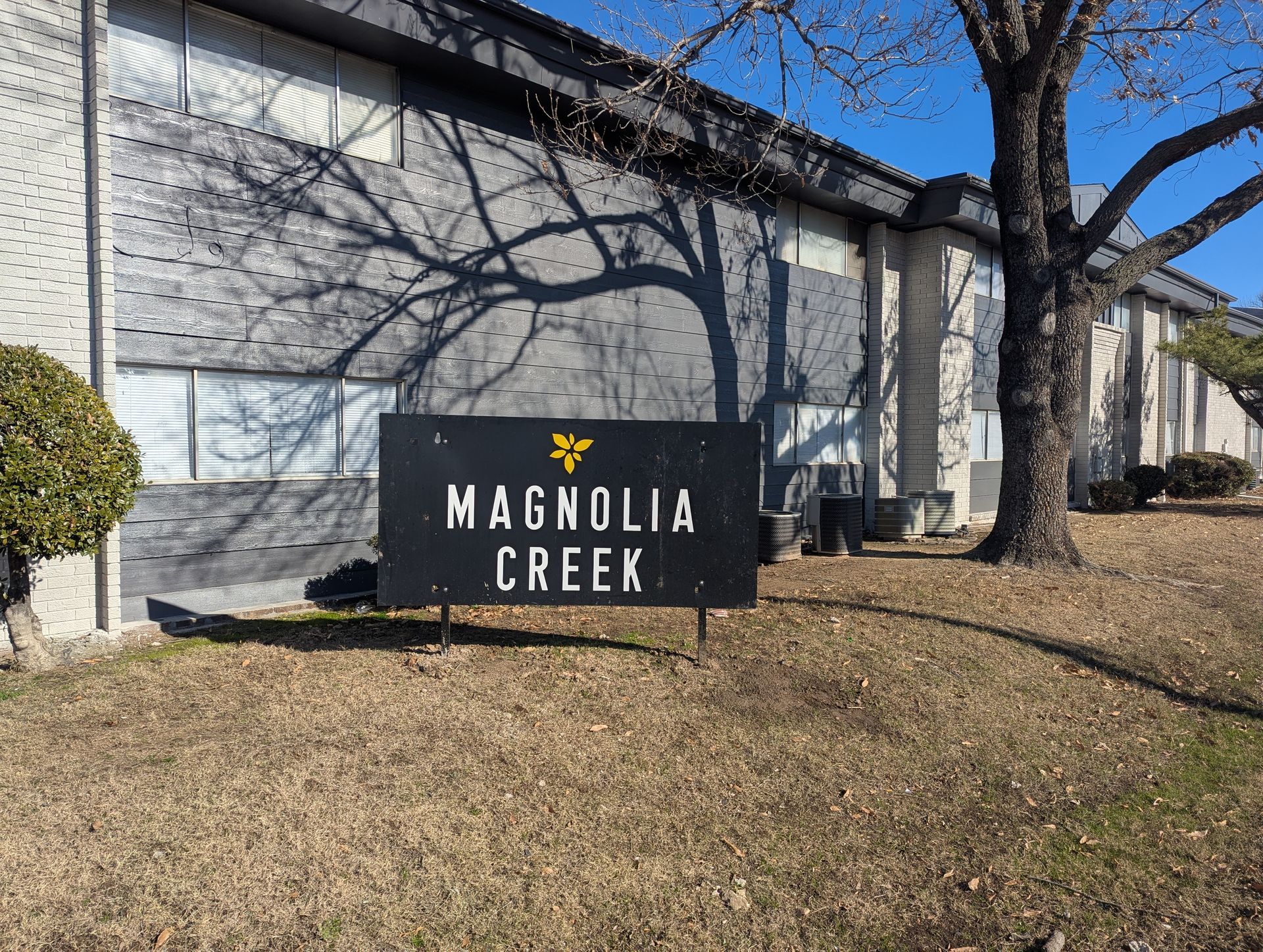 Magnolia Creek sign in front of a gray building with tree shadows on a sunny day.