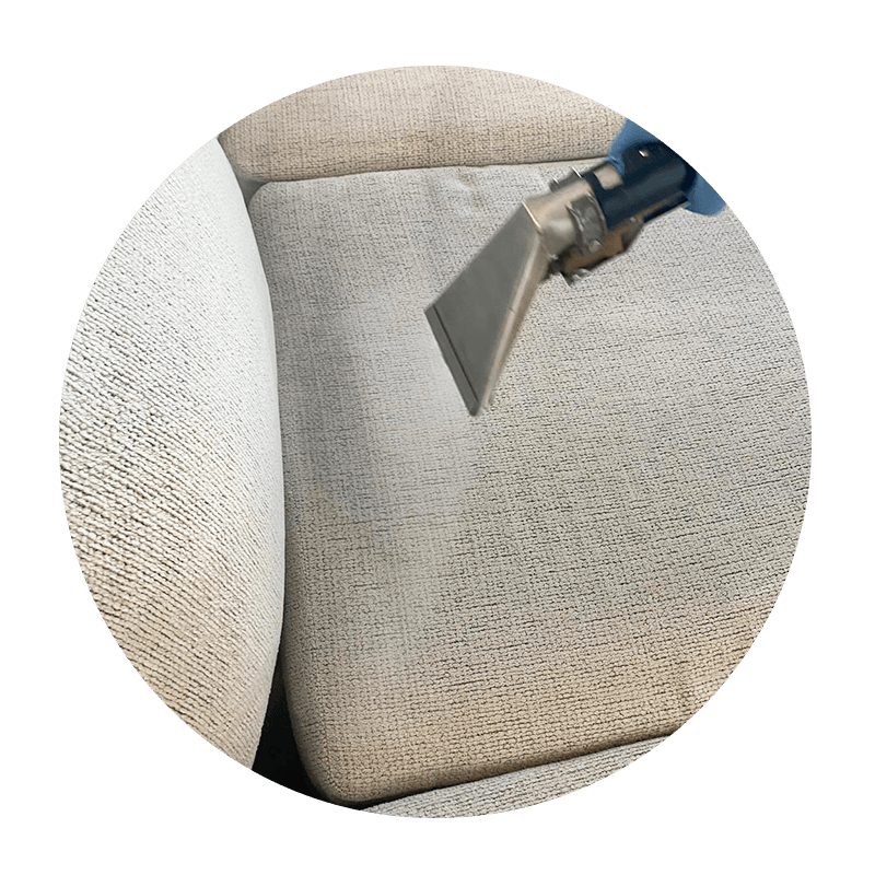 A person is cleaning a couch with a vacuum cleaner.