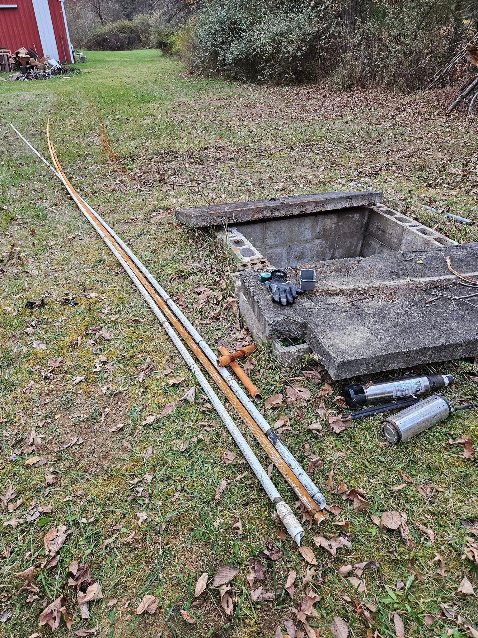 A bunch of pipes are laying on the ground next to a manhole cover.
