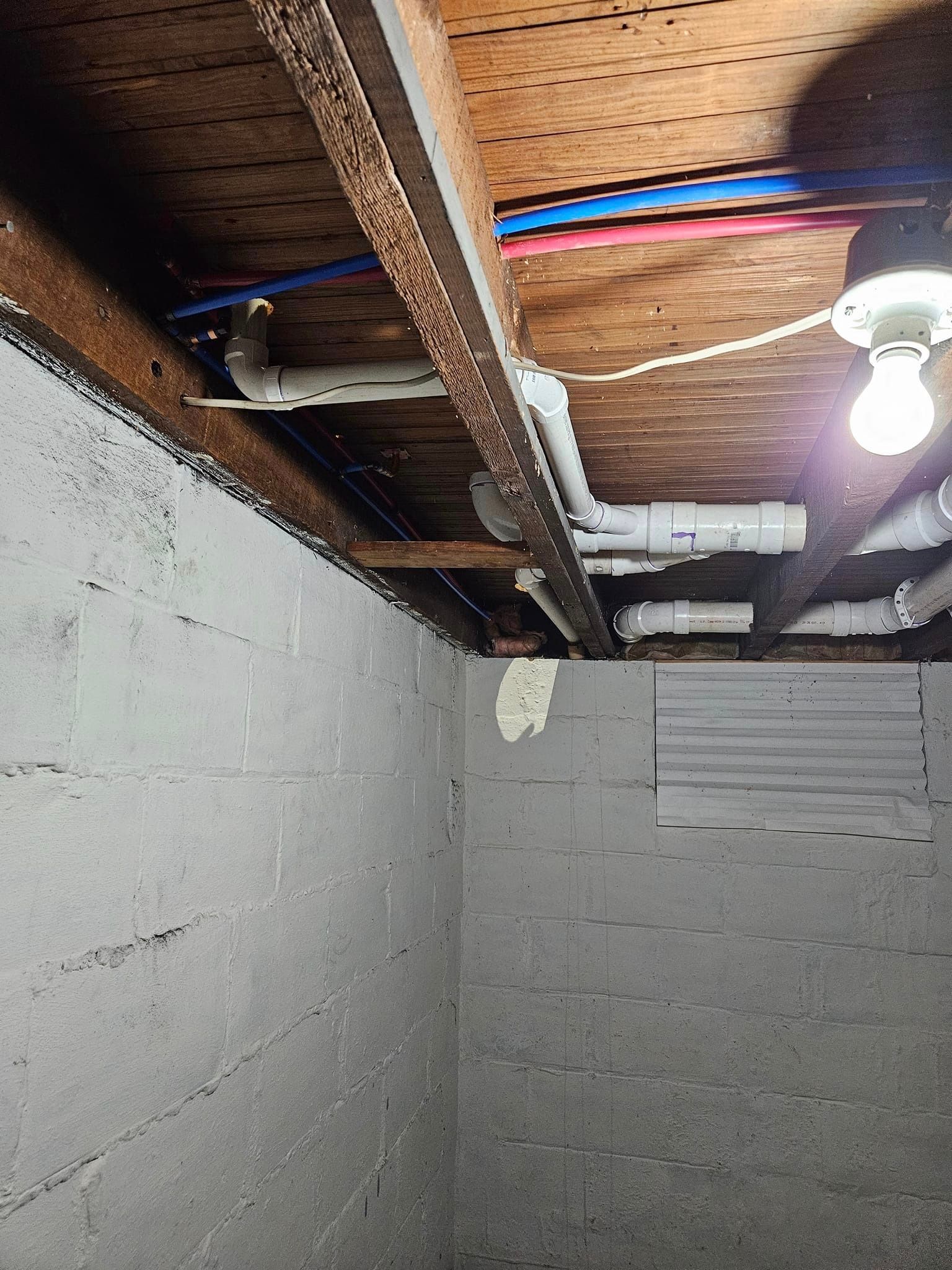 A basement with pipes and a light on the ceiling.