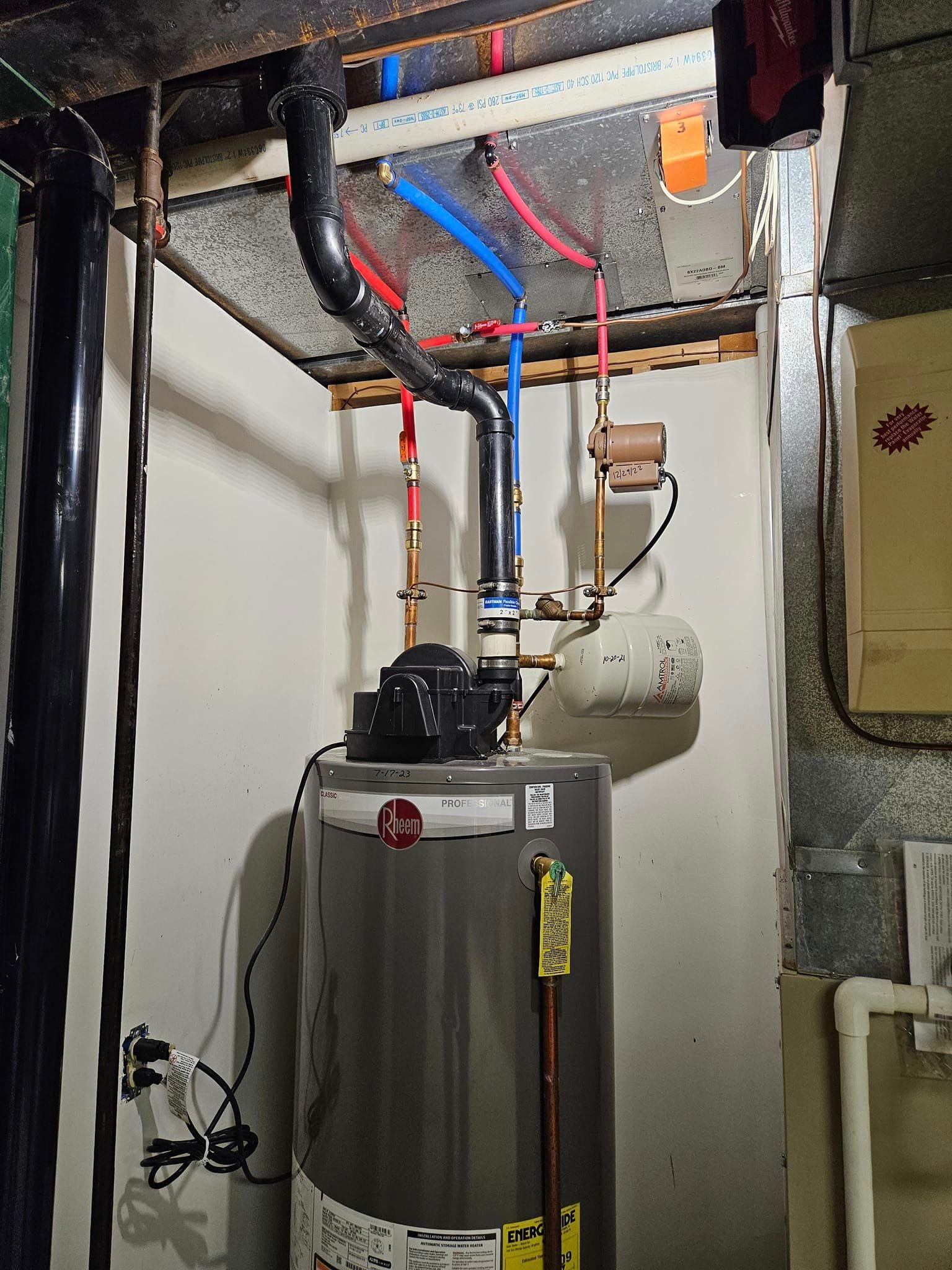 A water heater is sitting in a basement next to pipes.