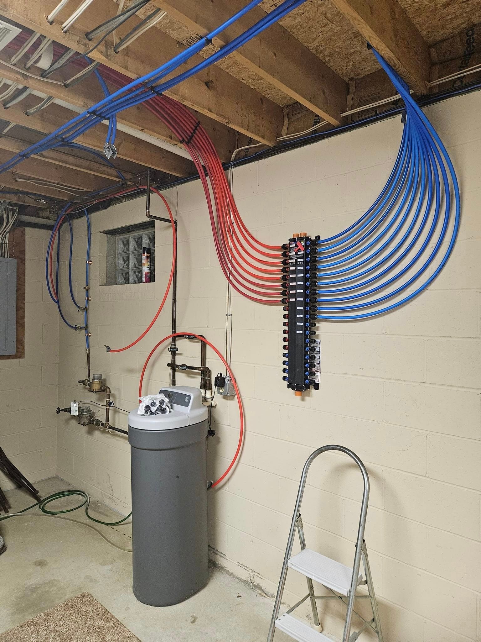 A room with a trash can , ladder , and lots of wires hanging from the ceiling.