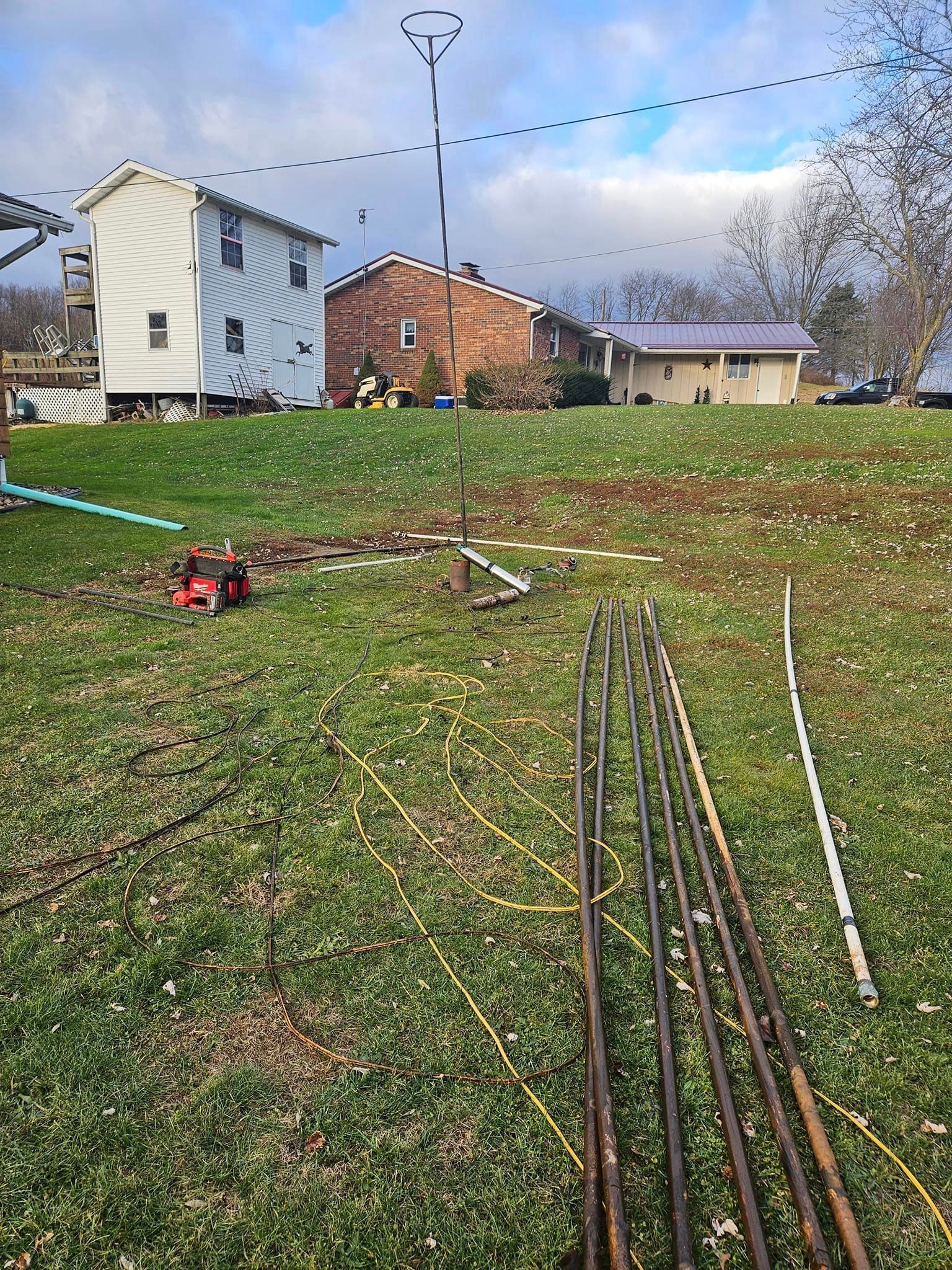 A row of metal pipes are sitting in a grassy field in front of a house.