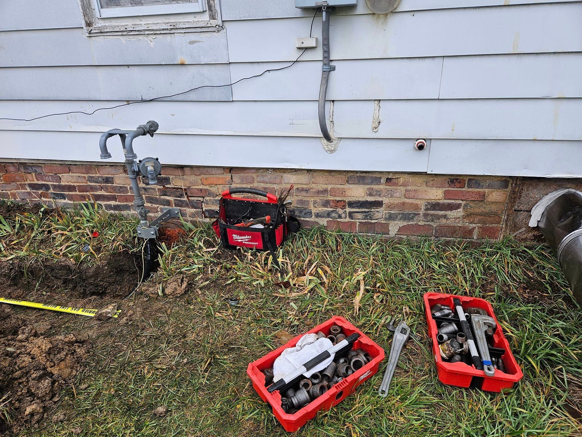 A plumber is working on a faucet outside of a house.