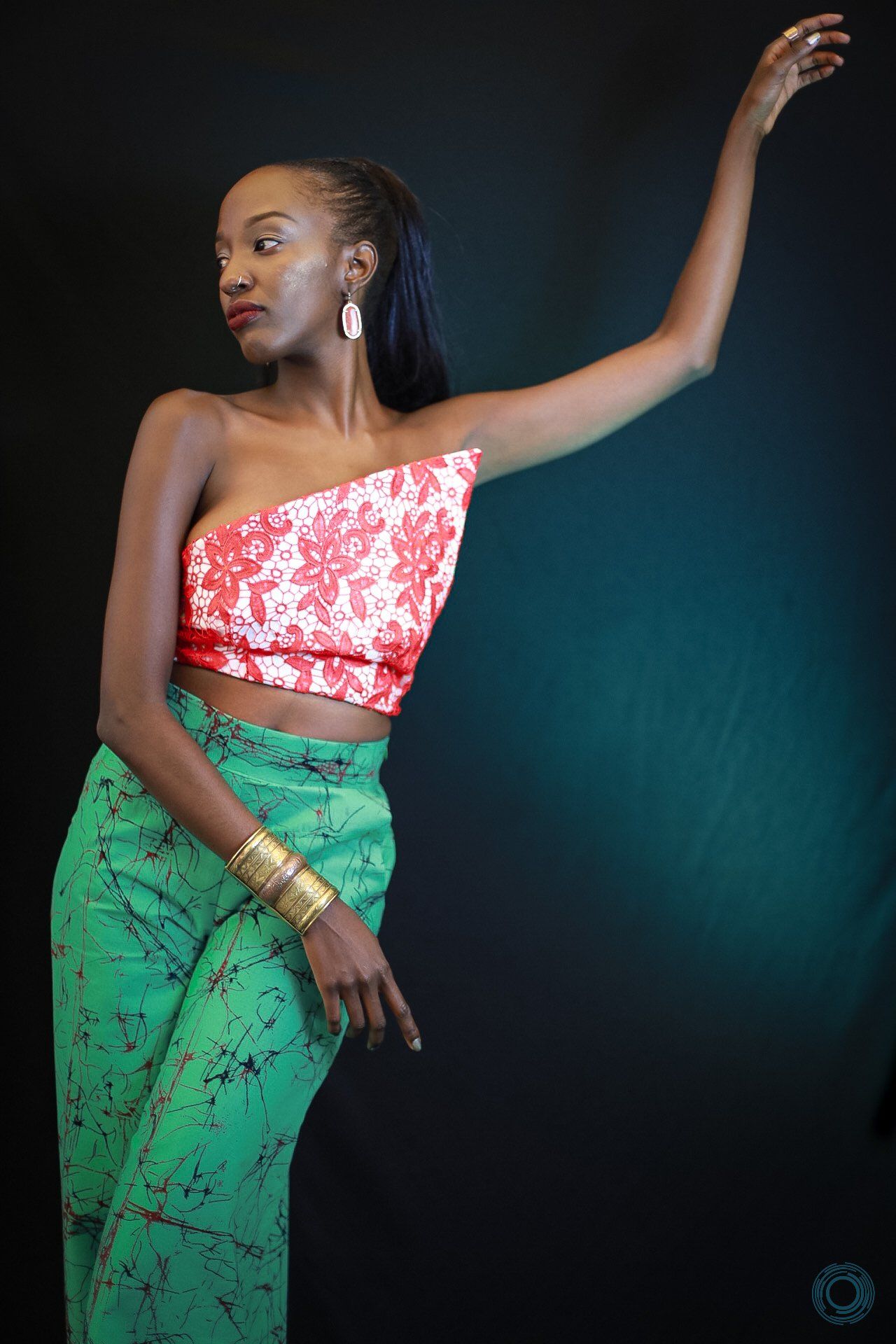 A woman is wearing a red and white crop top and green pants.