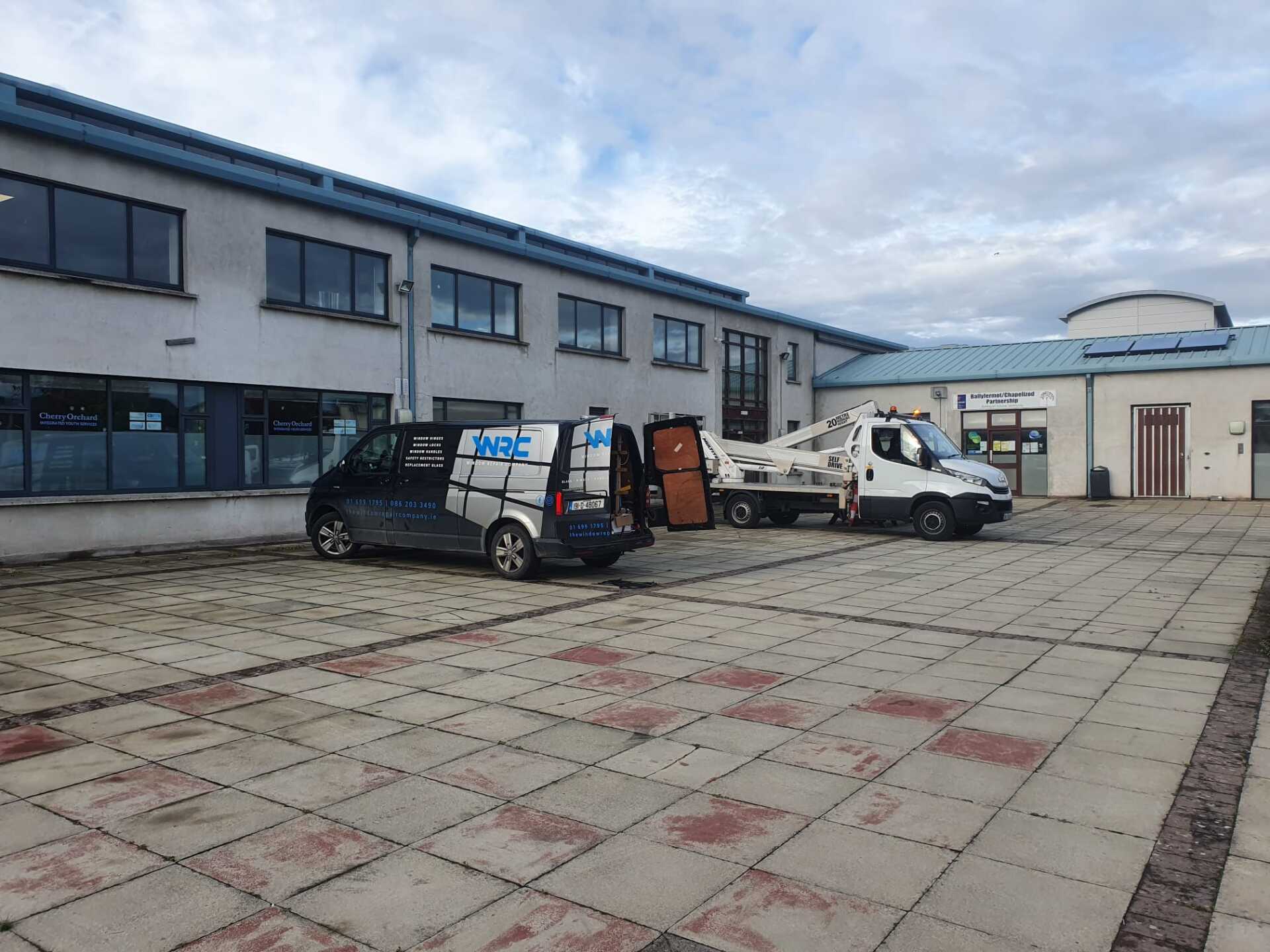 Two vans are parked in front of a large building.