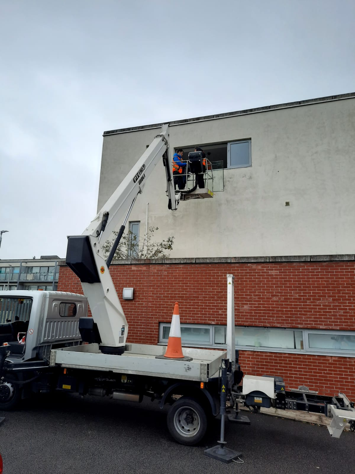 A white truck with a crane on the back is parked in front of a brick building